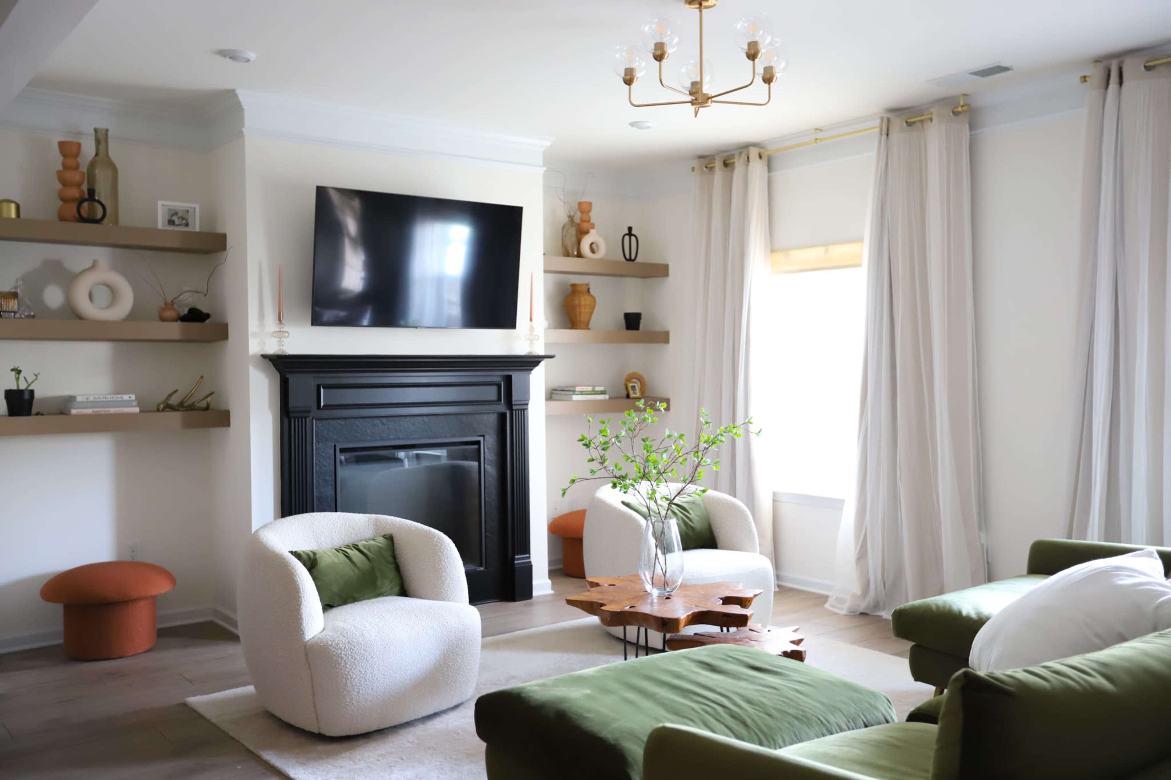 A modern living room features a black fireplace, a television mounted on the wall, and green seating arranged around a wooden coffee table.
