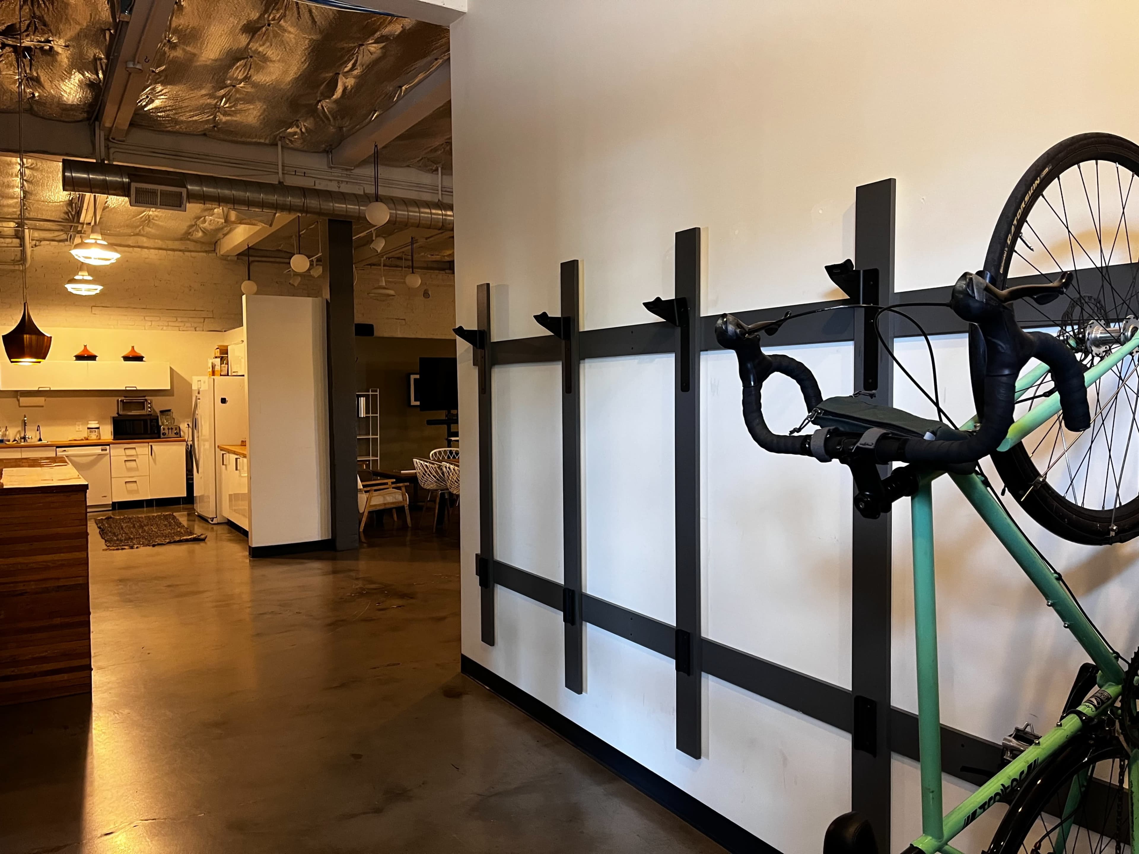 The image shows a modern interior space with a kitchen in the background, featuring a bike mounted on a wall rack.