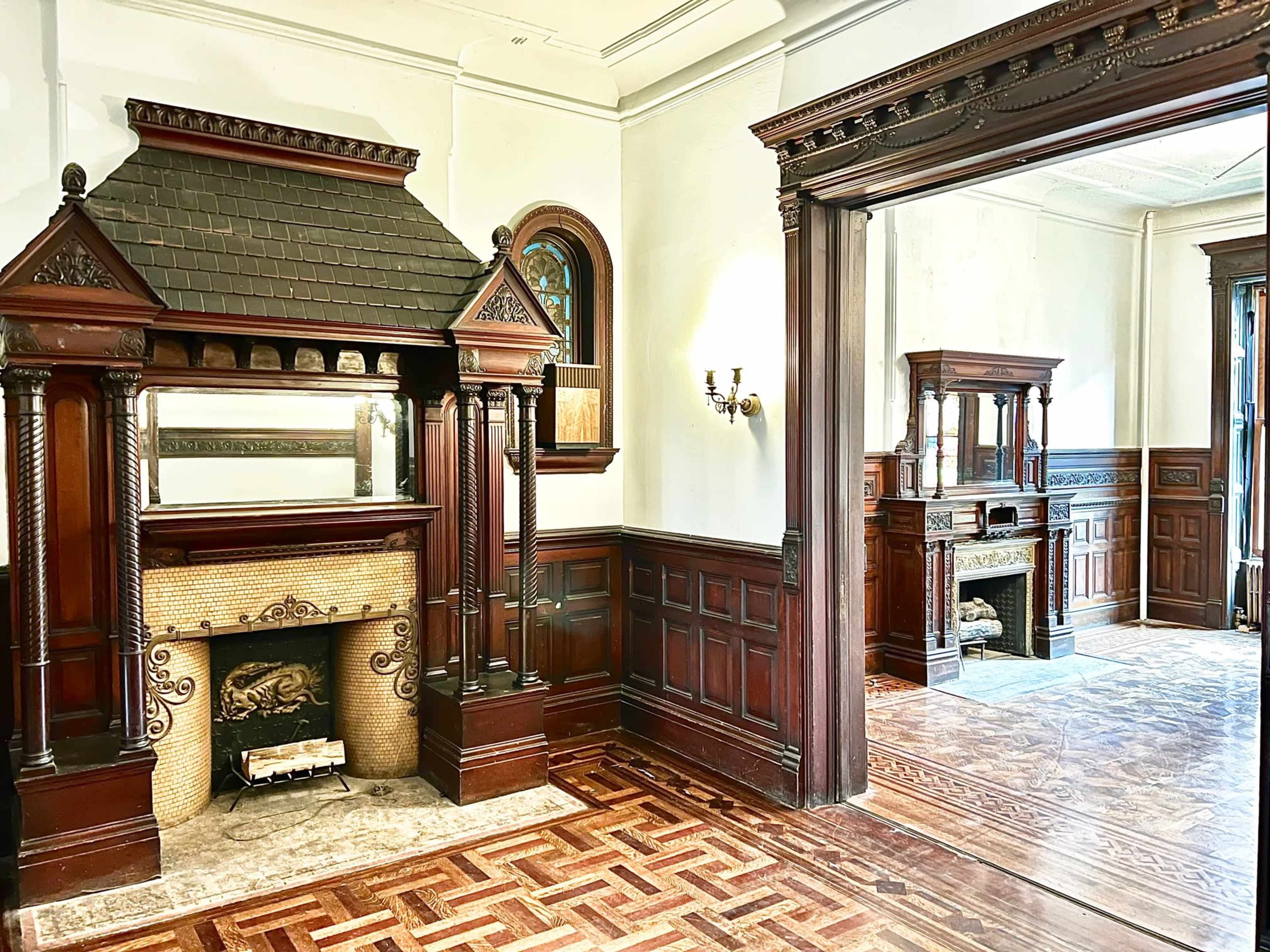 The image shows a vintage interior featuring ornate wooden paneling, intricate mantelpieces, and decorative details in a spacious room.