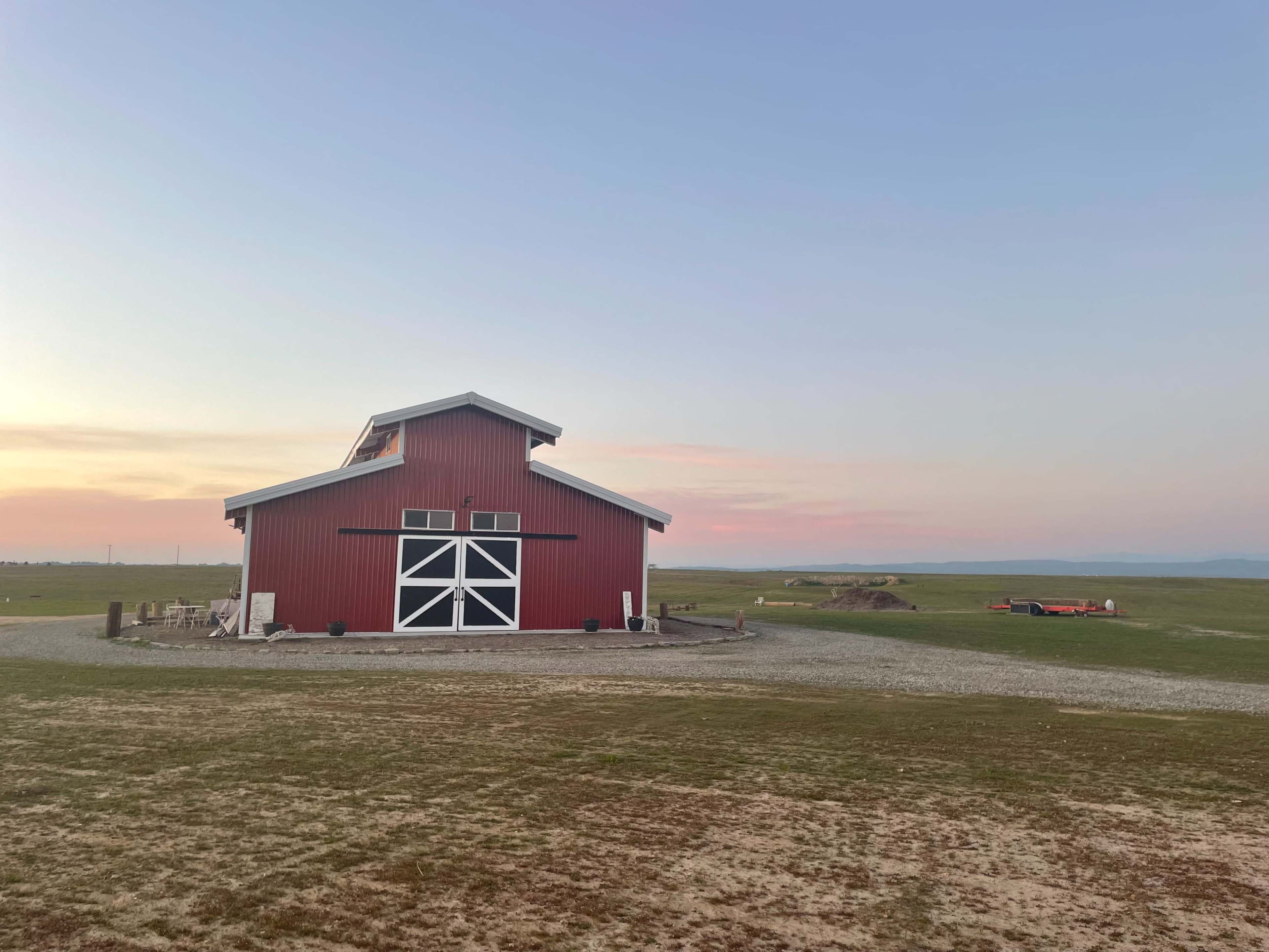 A red barn stands on a grassy field under a pastel sky.