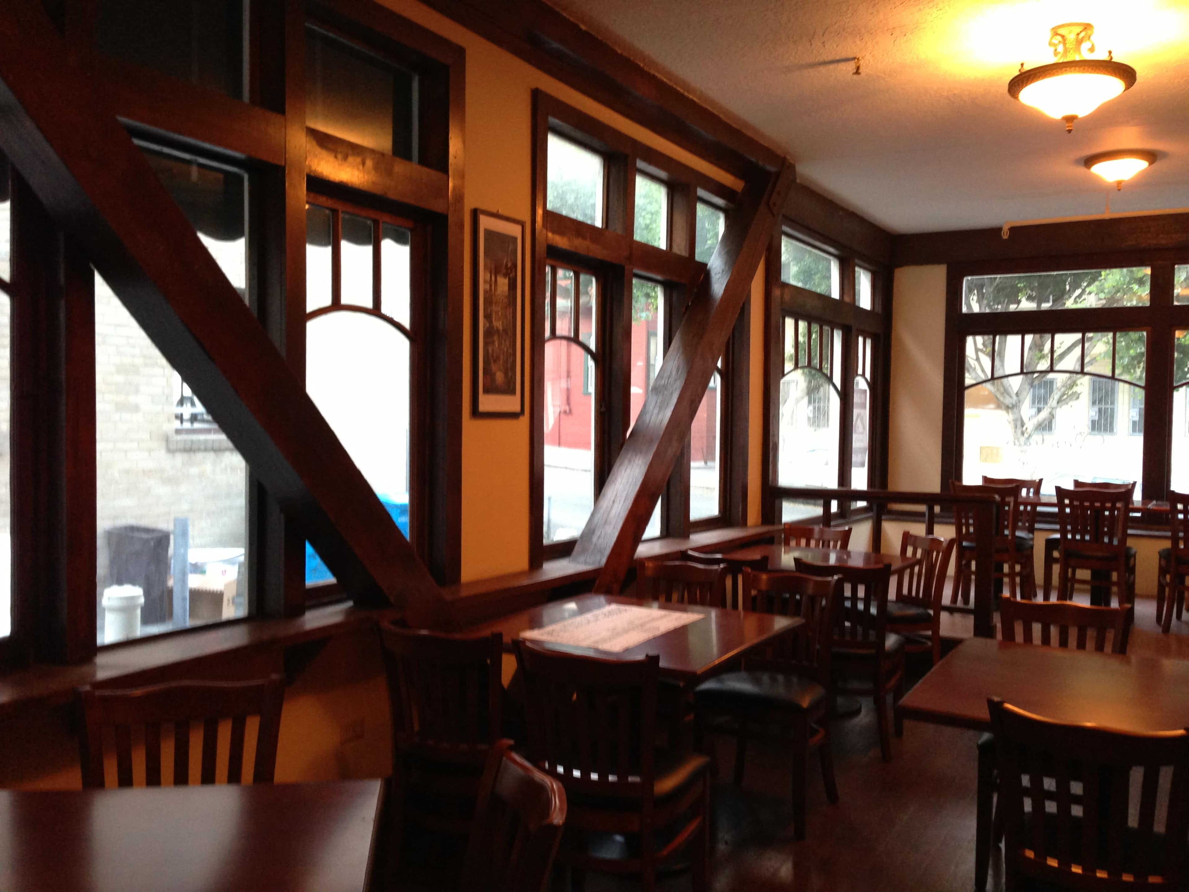 The interior of a restaurant featuring wooden beams and several tables arranged near large windows.