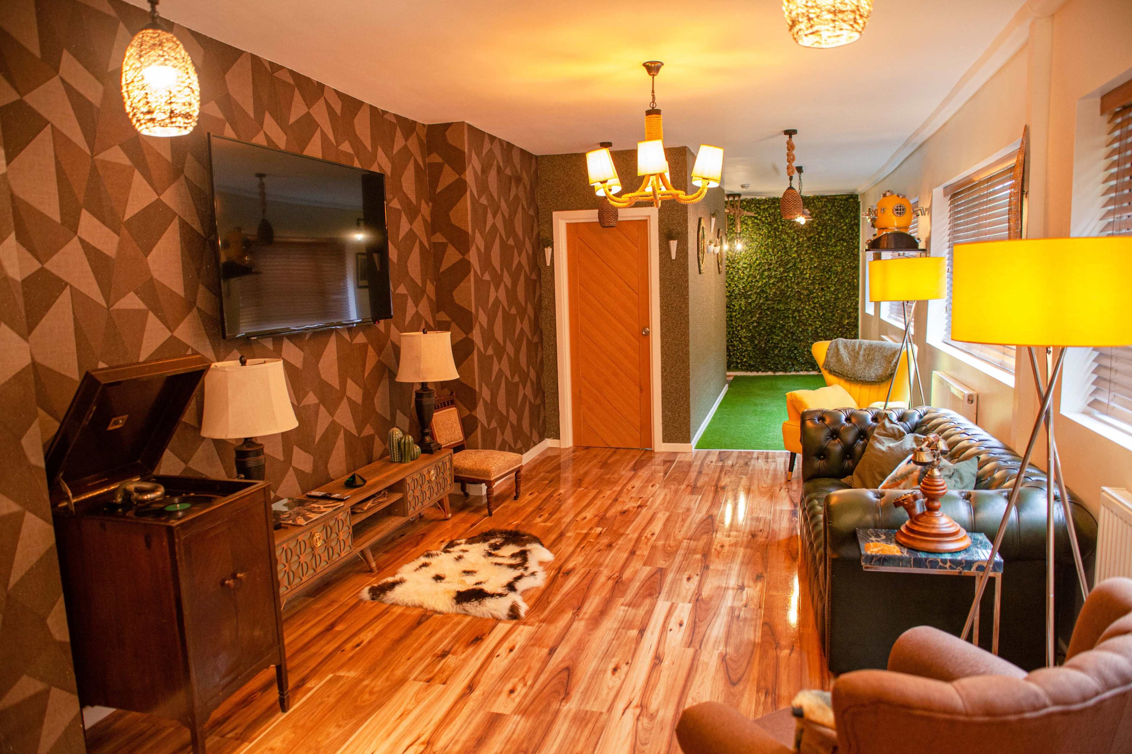 A modern living room featuring wooden flooring, a large TV mounted on a patterned wall, and various decorative elements like lamps and a cowhide rug.