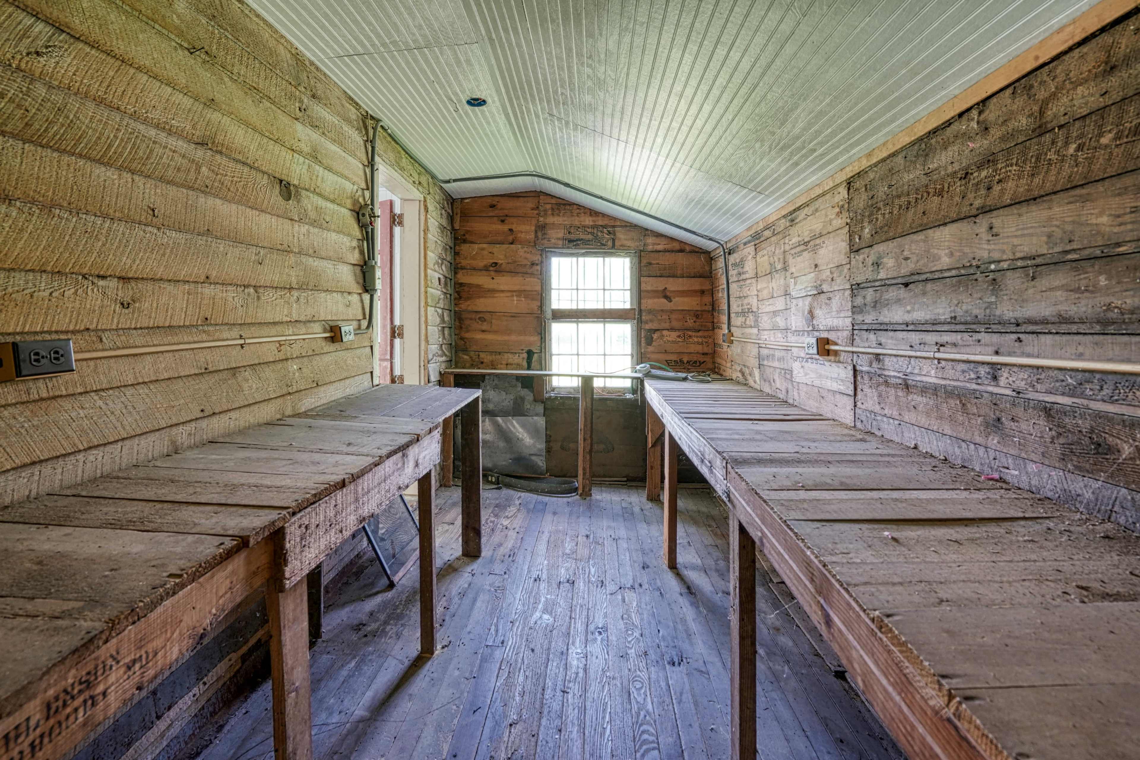 The image shows an empty wooden interior space with two long tables on either side and a window at the far end.