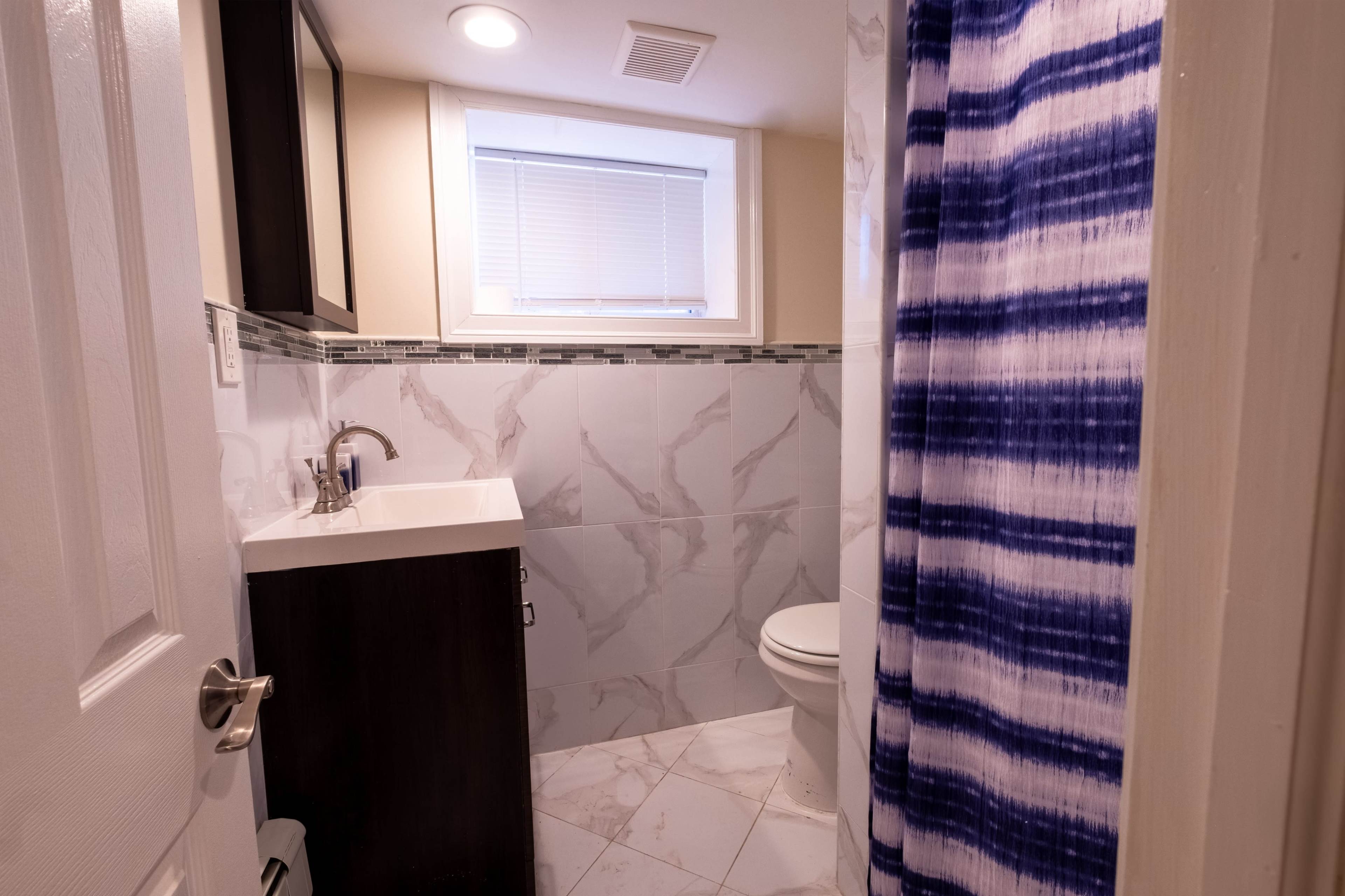 A small bathroom features a toilet, sink with storage, and a shower with a blue and white striped curtain.