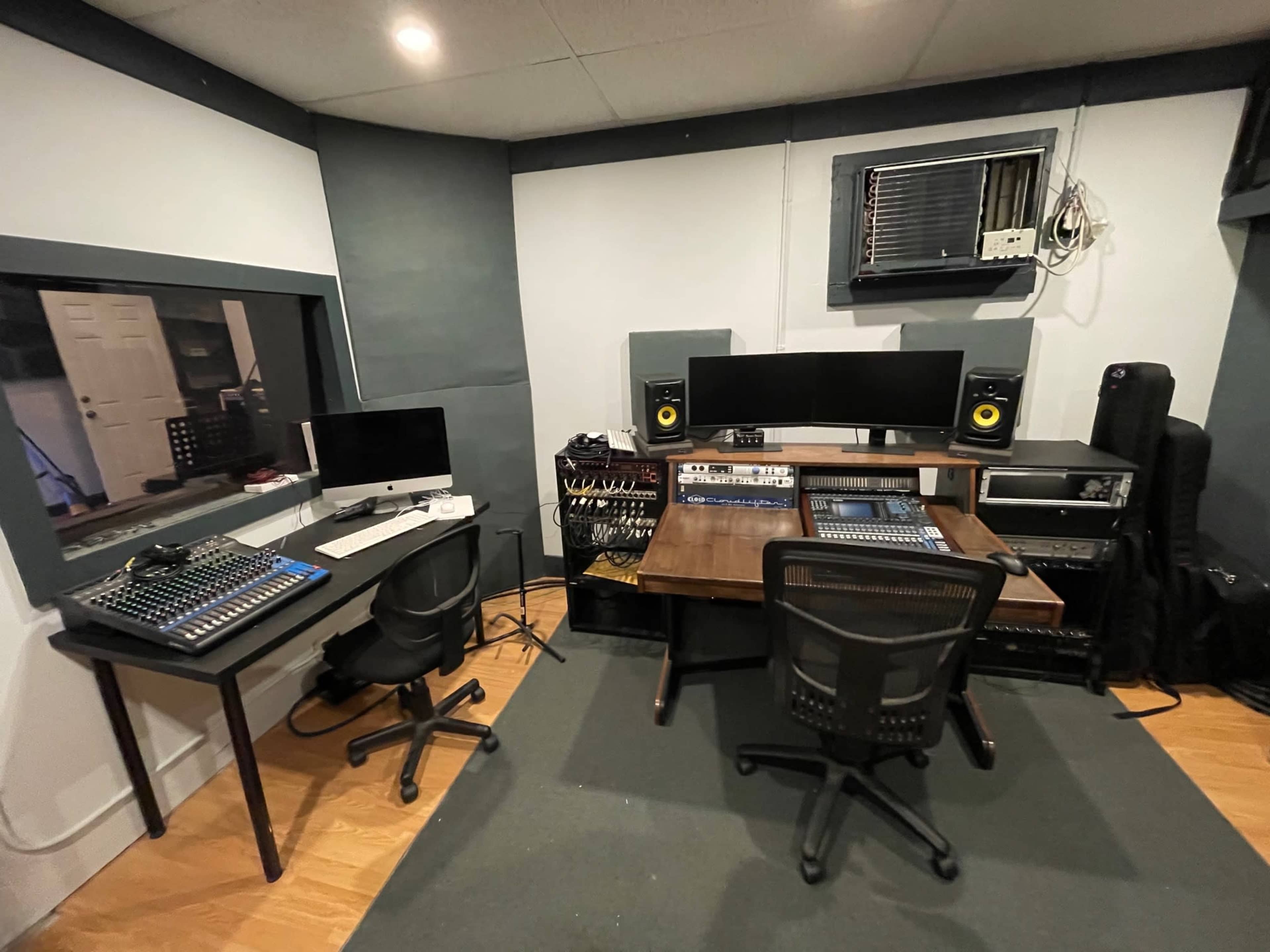 A modern audio recording studio featuring two workstations with computer monitors, speakers, and a central mixing console.