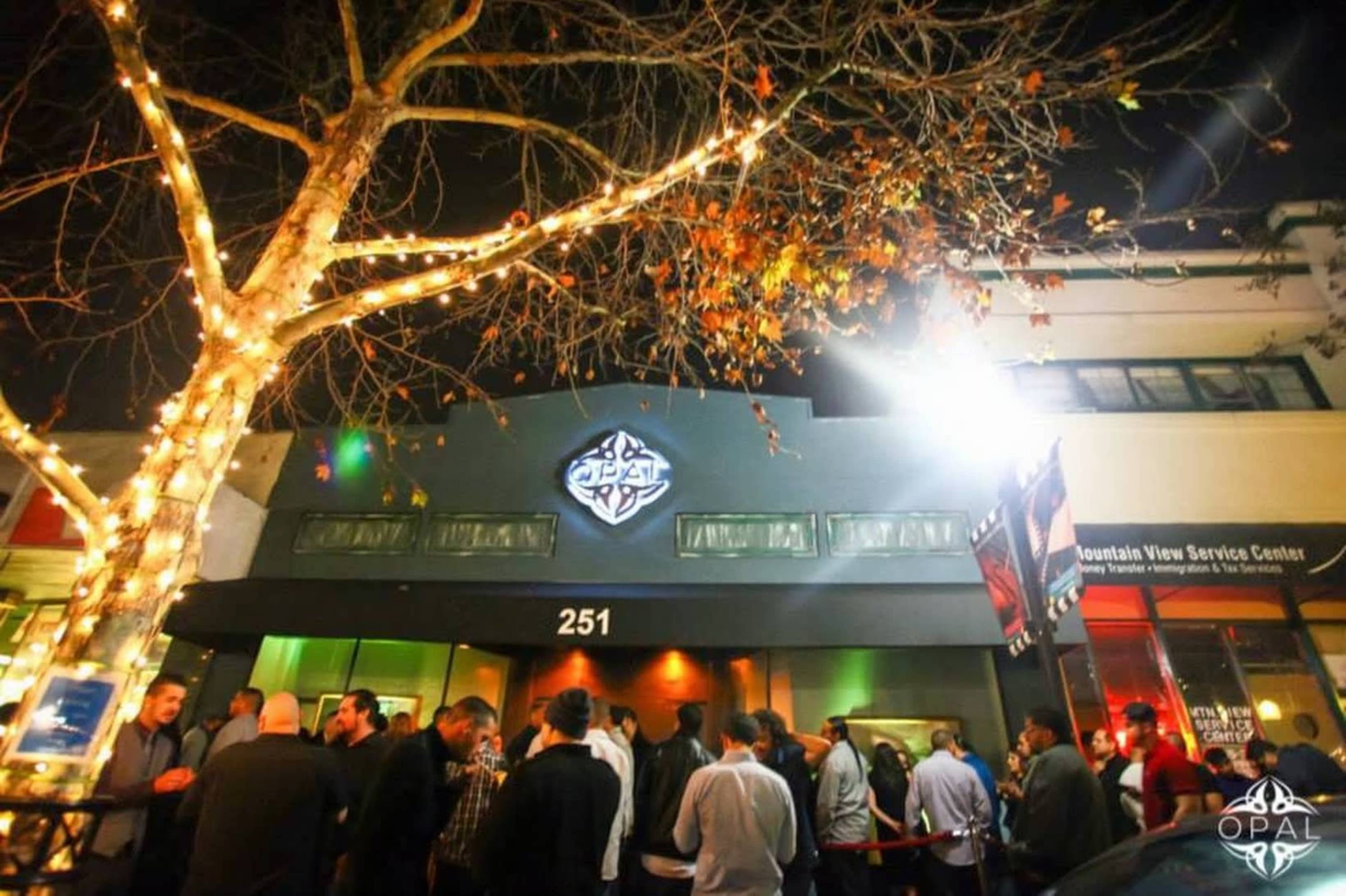 A crowd of people is gathered outside a dimly lit building with prominent signage at night.