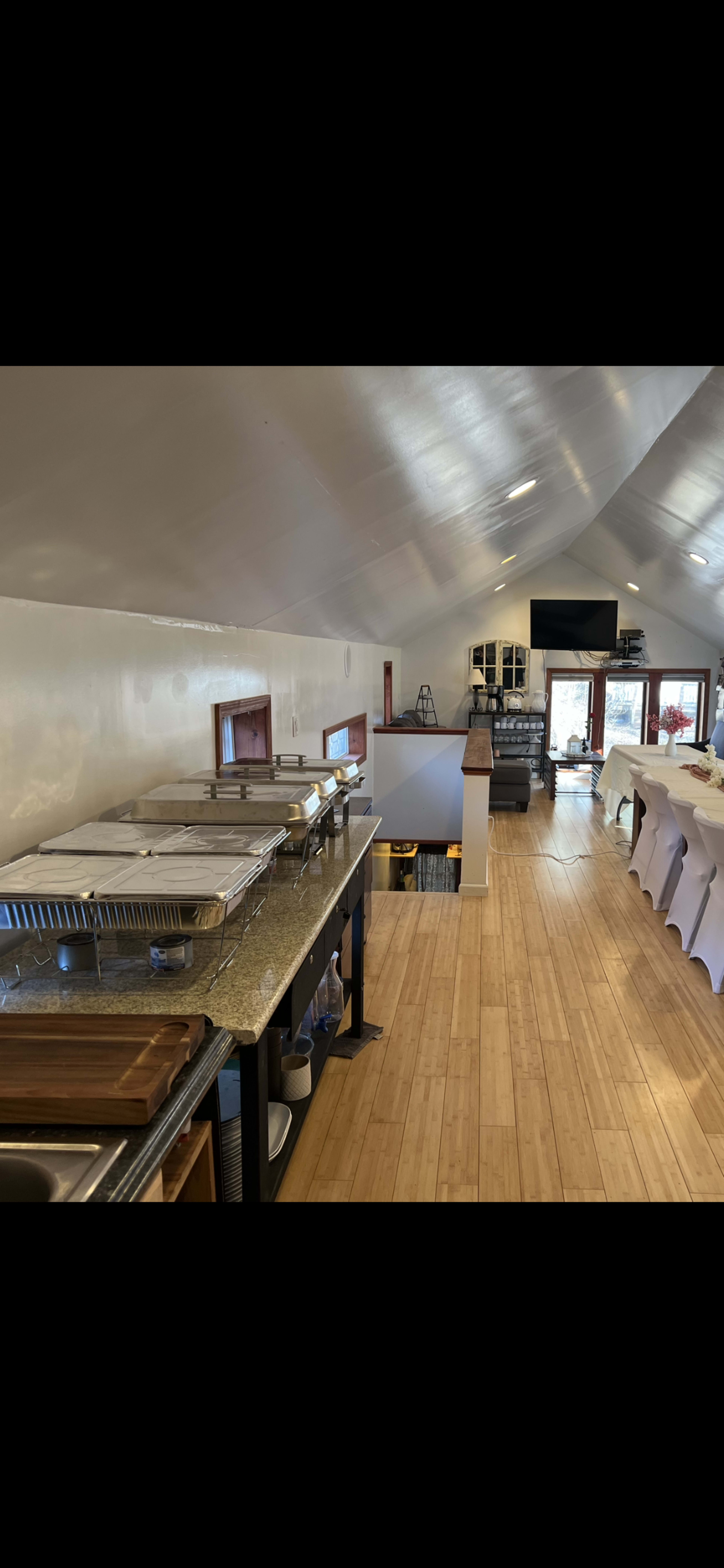 The interior of a spacious dining area with a buffet setup, featuring metal trays on a counter and a wooden floor.