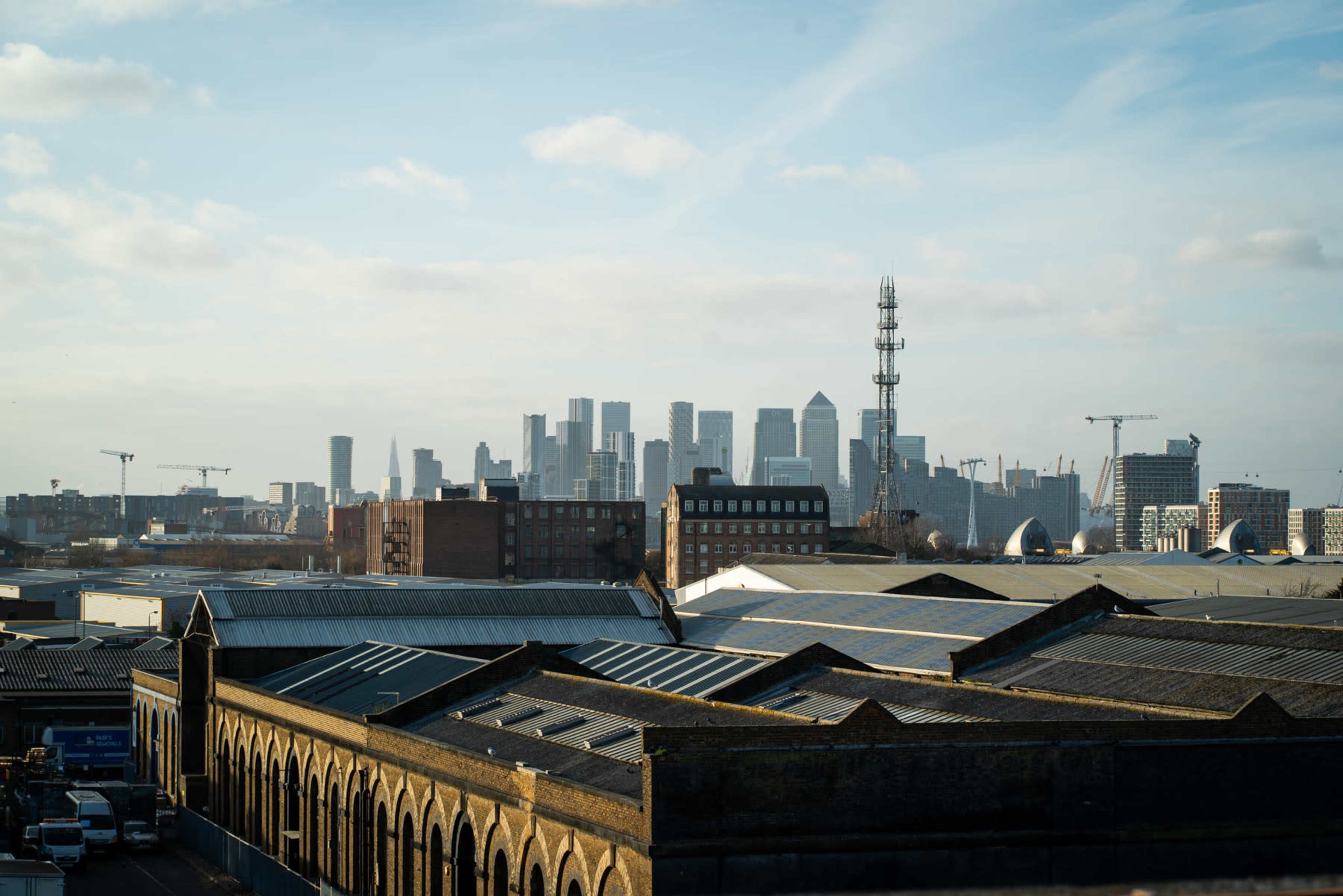 A city skyline with tall buildings and telecommunications towers, viewed from a low vantage point with industrial rooftops in the foreground.