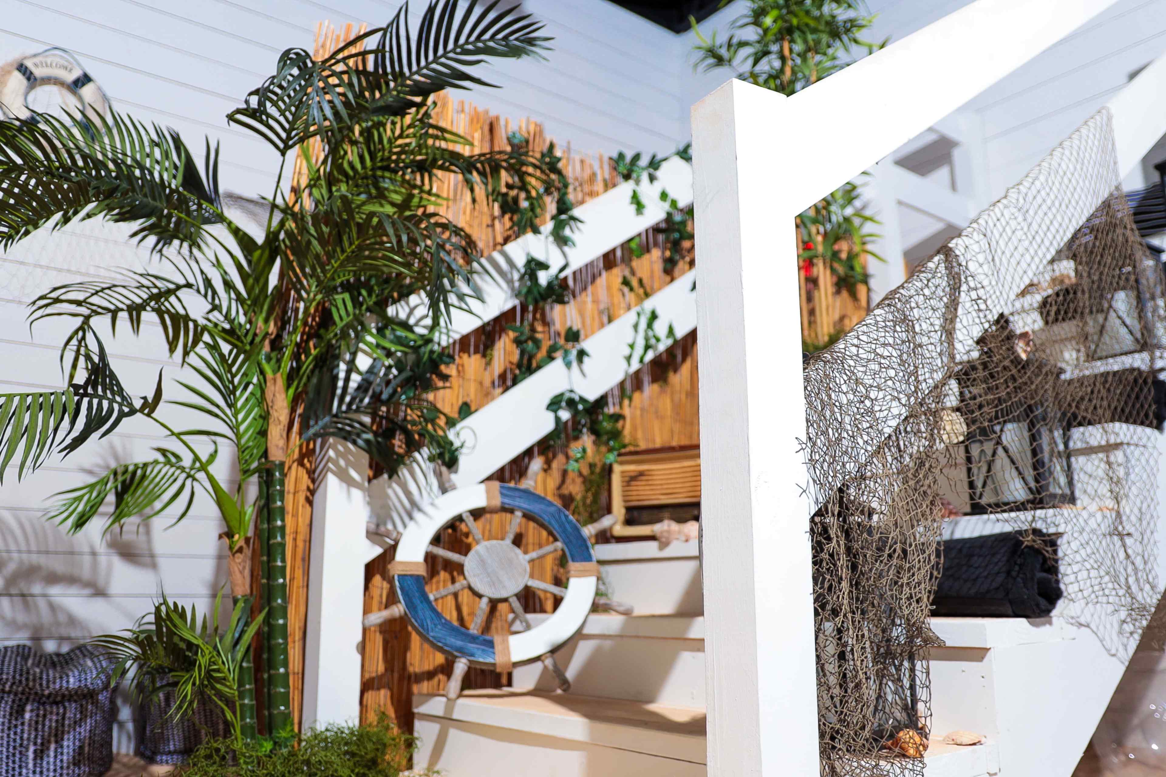 A staircase is adorned with a wooden railing, decorative plants, a life preserver, and nautical-themed decor.