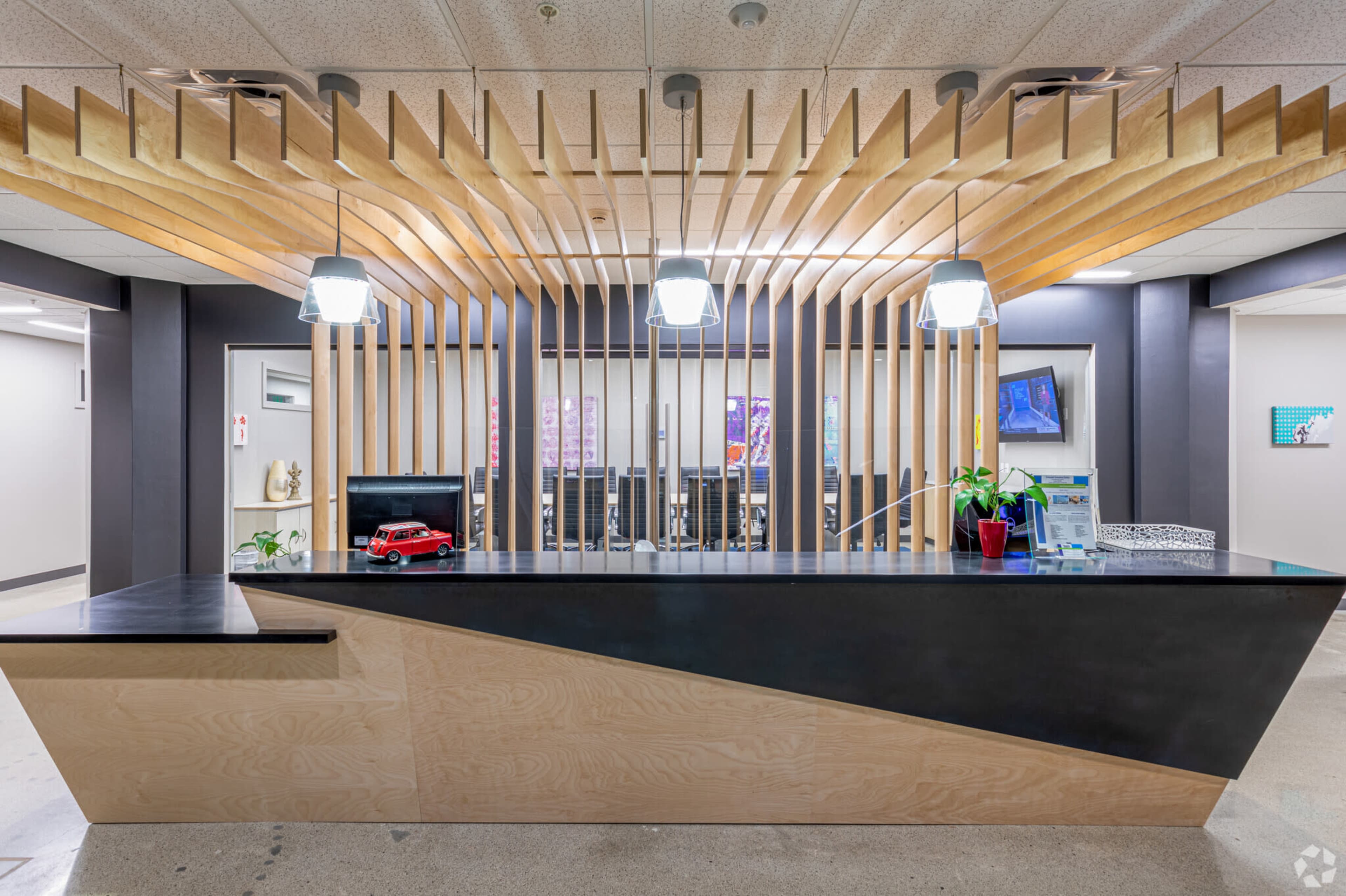 A modern reception desk with a wooden feature wall and pendant lighting, situated in a bright, open office space.