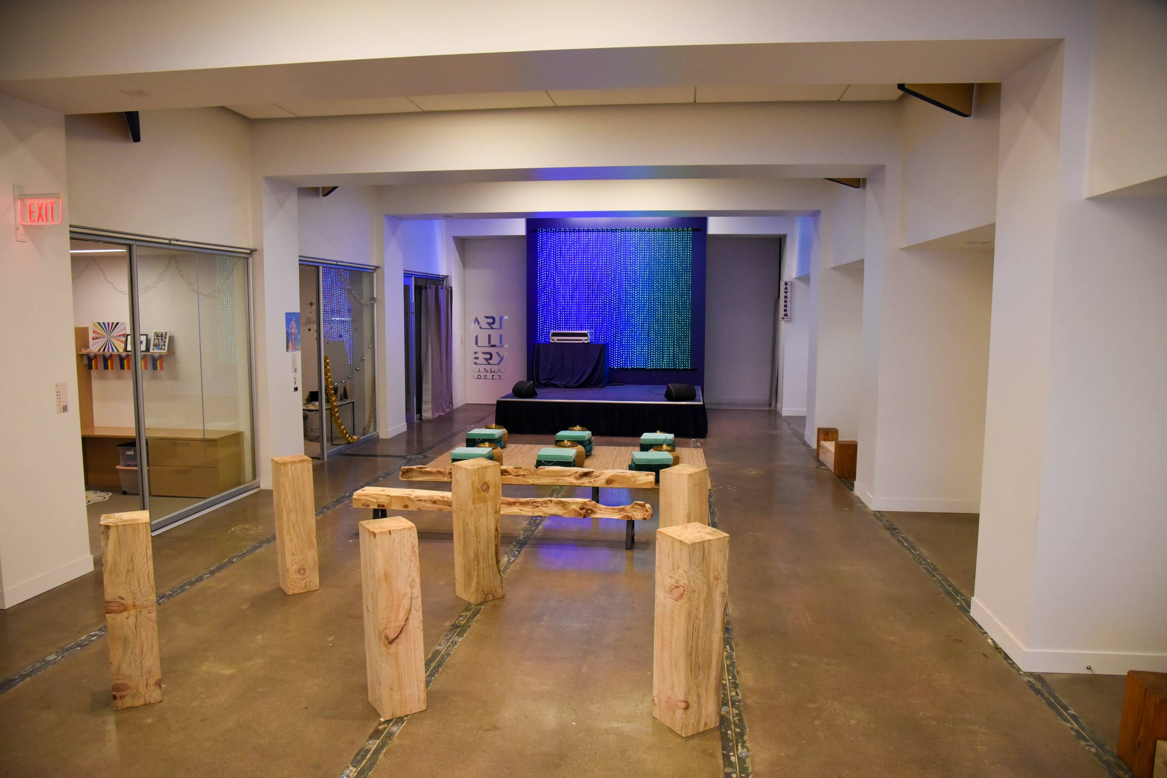 A spacious indoor area with a simple wooden seating arrangement and a small stage lit with blue lighting at one end.