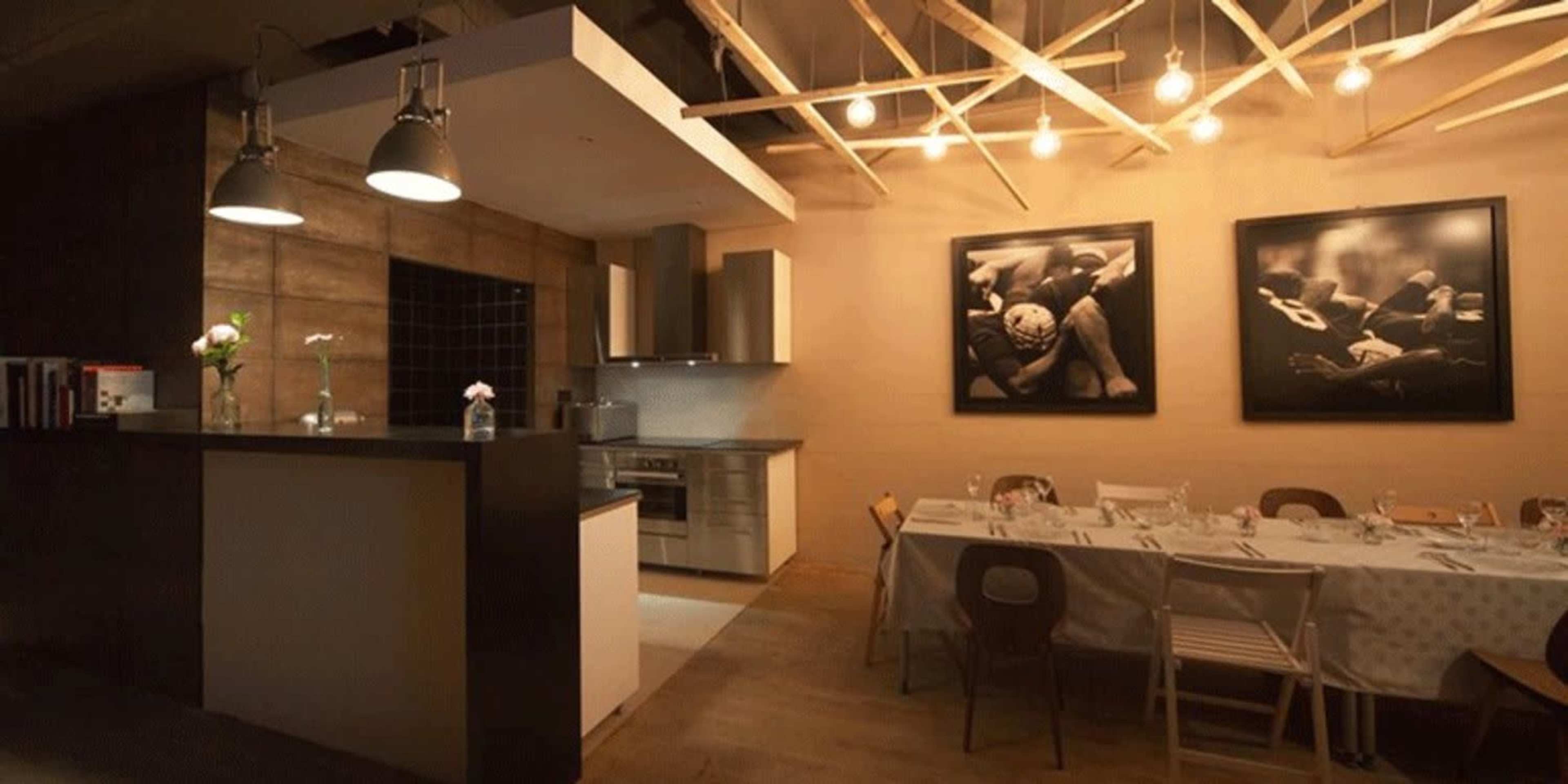 A modern kitchen area with a long dining table set up, illuminated by hanging light fixtures.