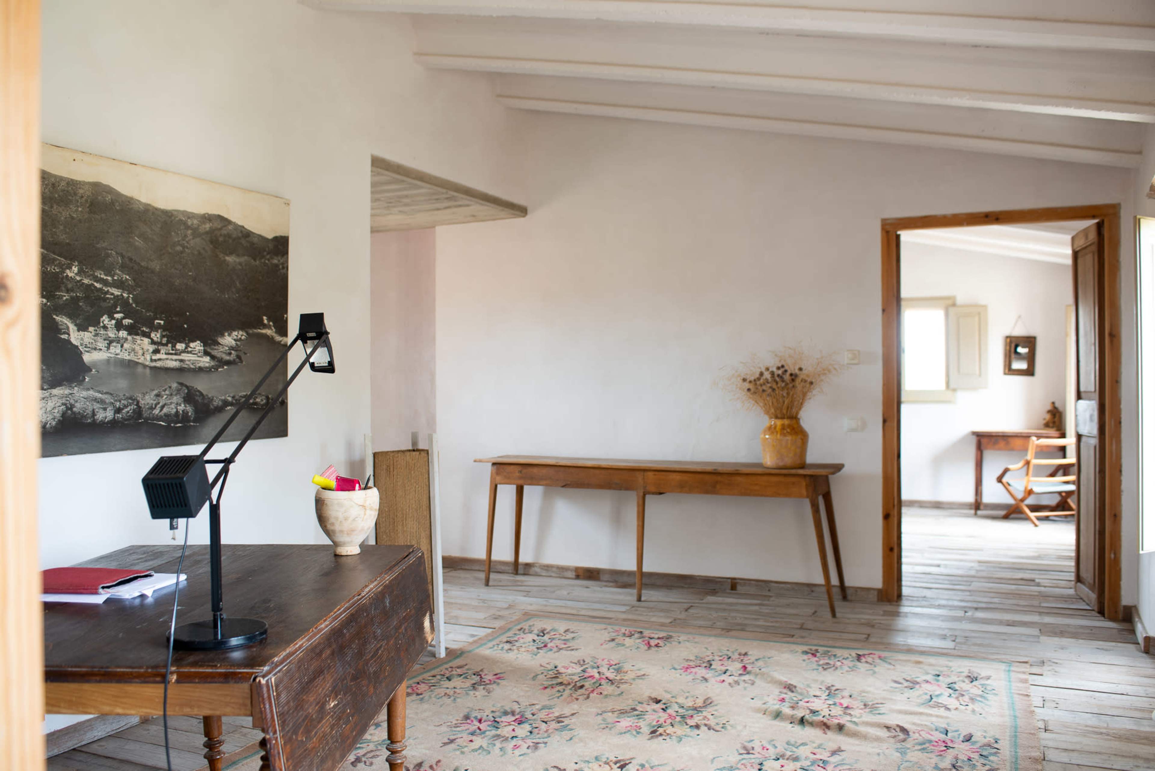 A simple interior space featuring a wooden table, a desk lamp, a patterned rug, and a wall adorned with a large black-and-white photograph.