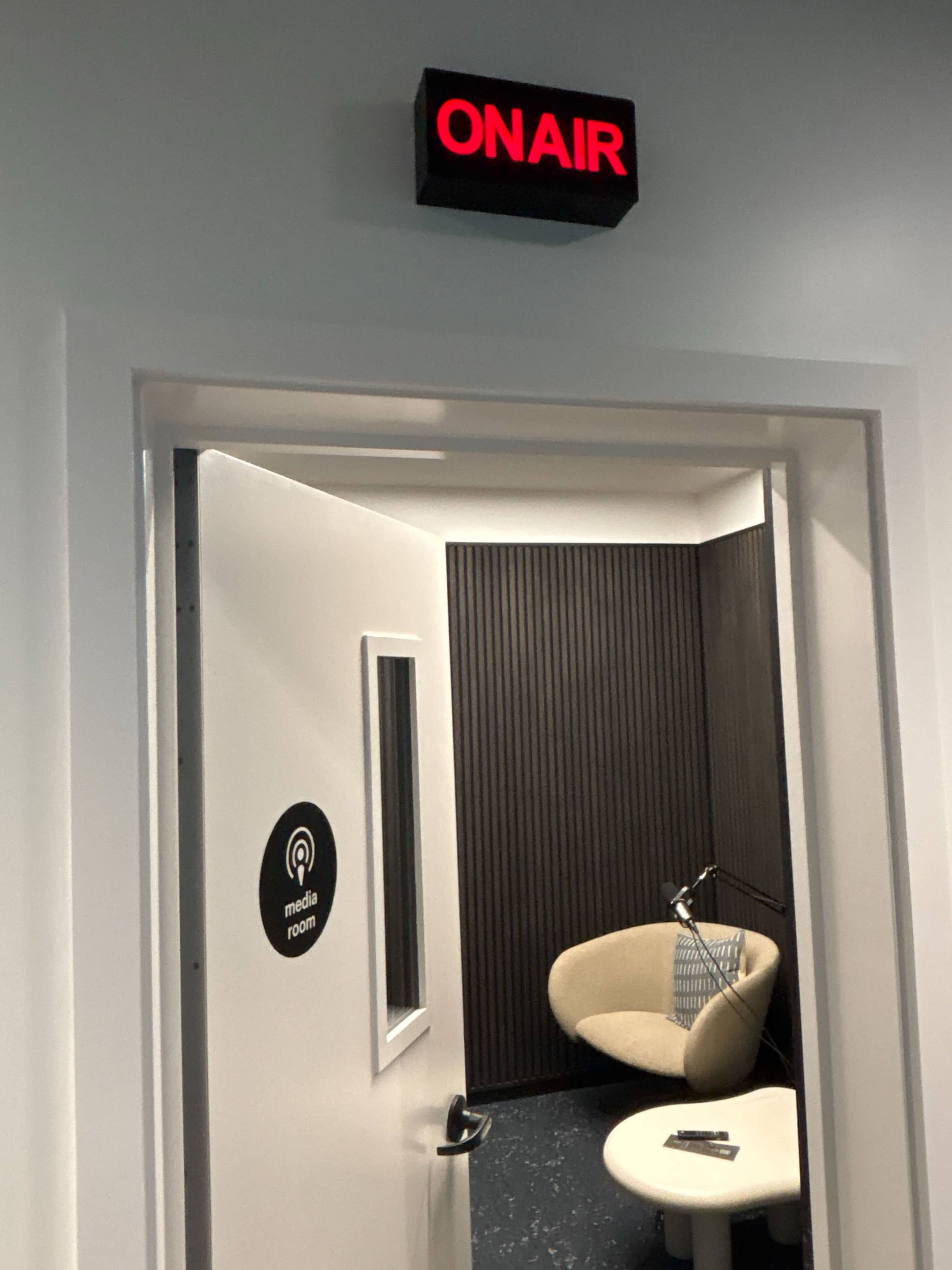 A door with a "ON AIR" sign leads to a small media room featuring a chair and a table.
