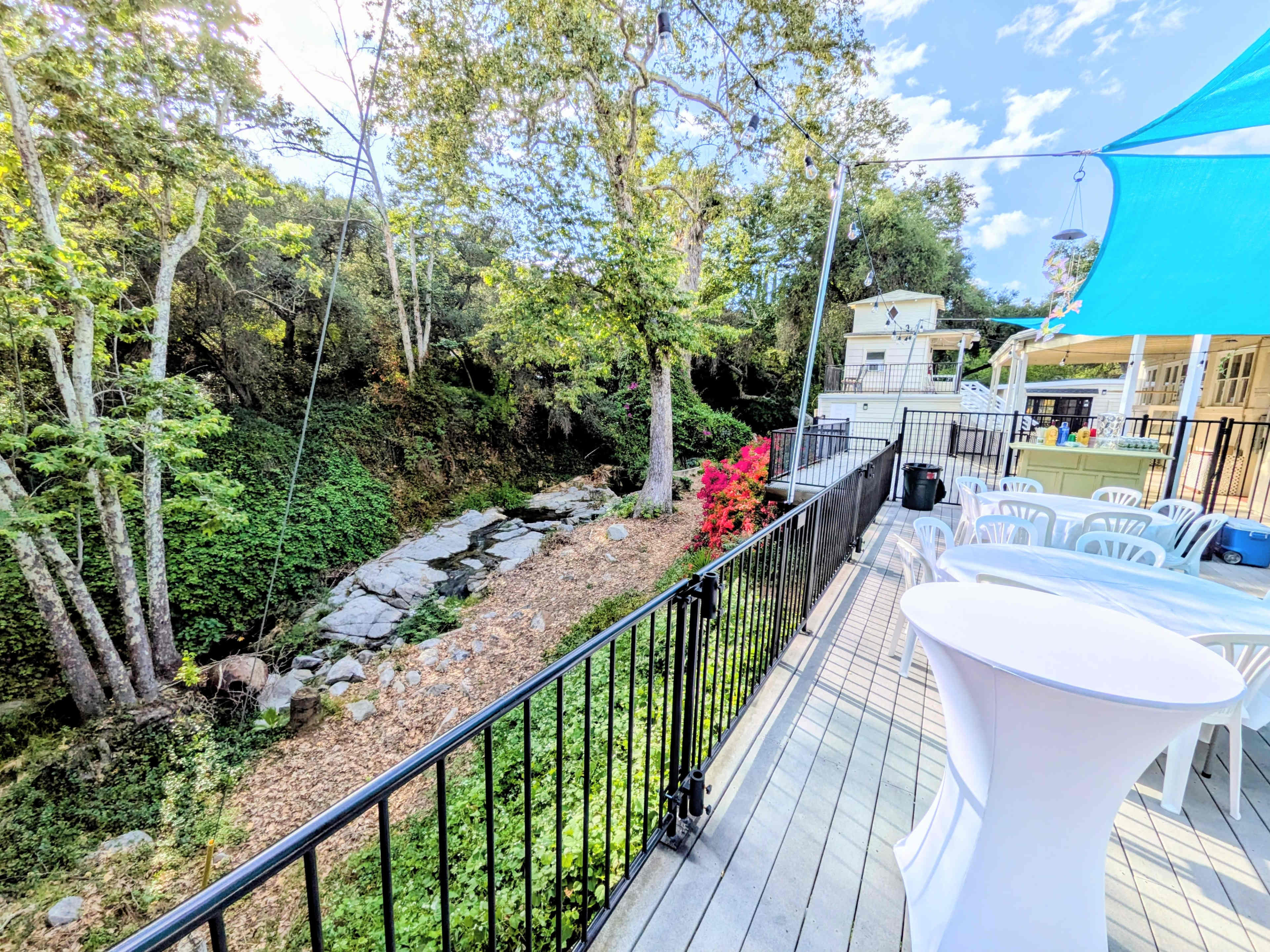 A patio area overlooks a stream bordered by greenery and rocks, with tables set up for an event in the background.