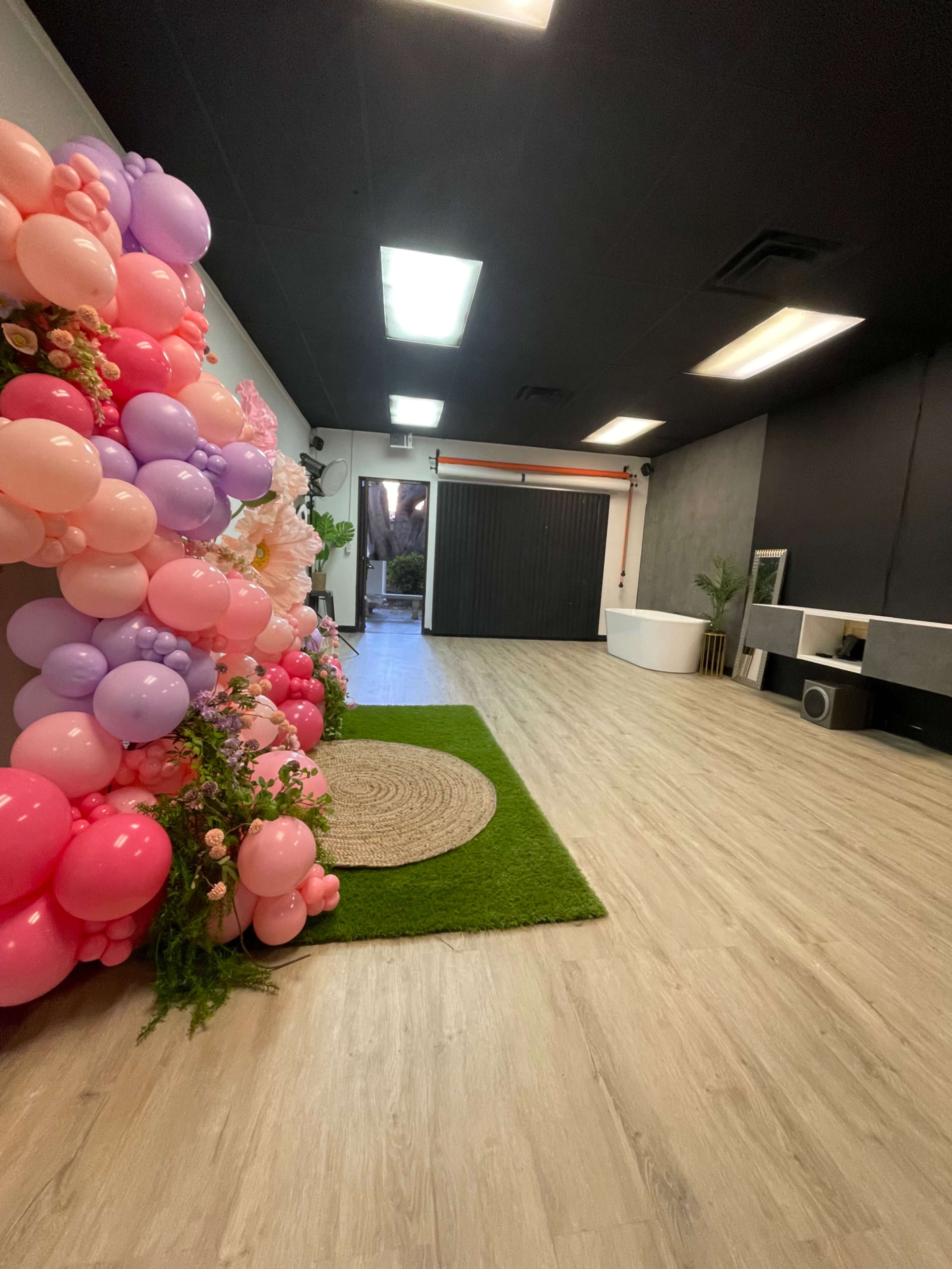 A spacious interior with a wall adorned with pink and purple balloons, a circular rug on a wooden floor, and a door leading outside.