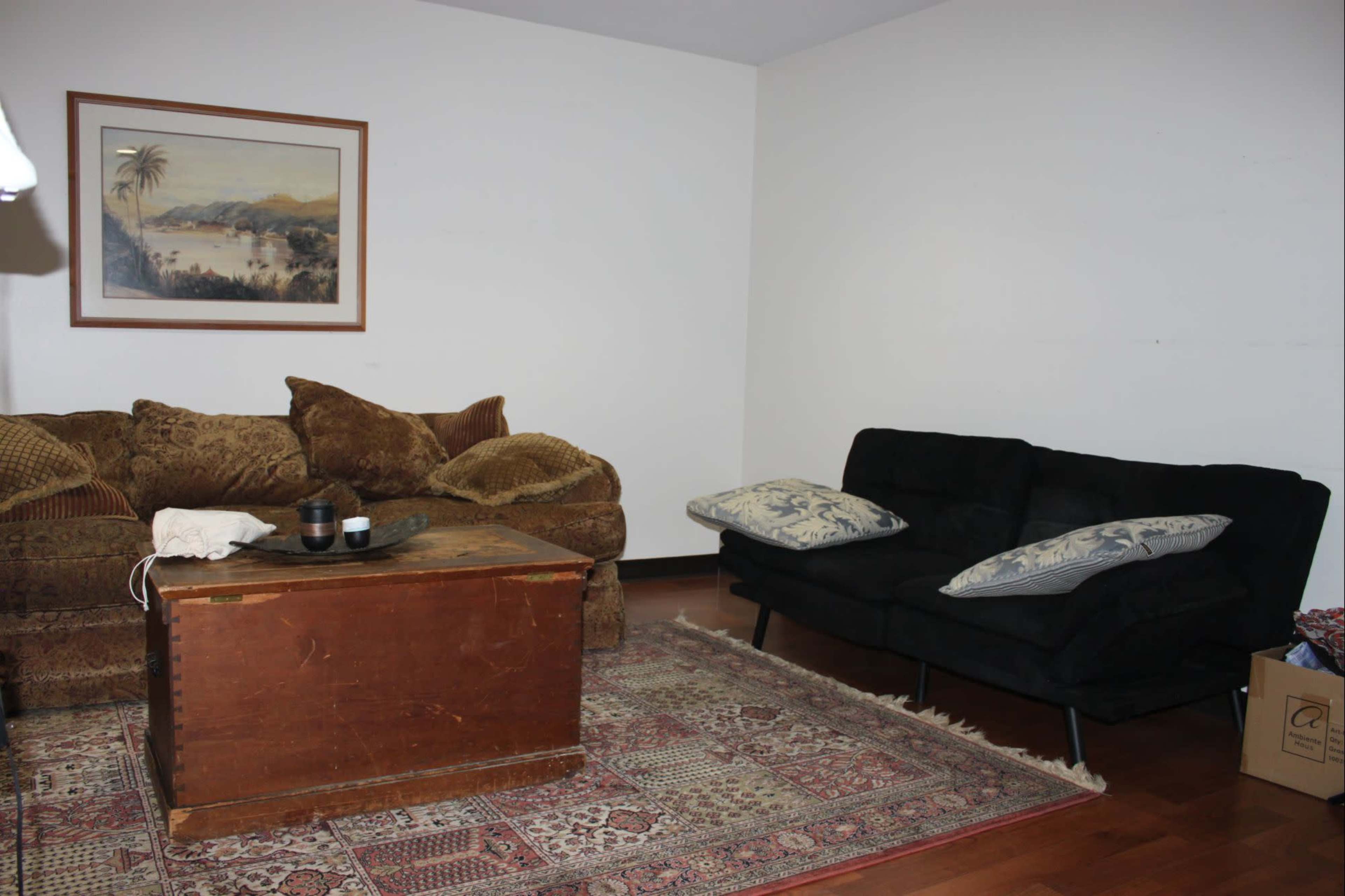 The image shows a living room with a wooden coffee table, a brown couch, a black loveseat, and a patterned rug on the wooden floor.