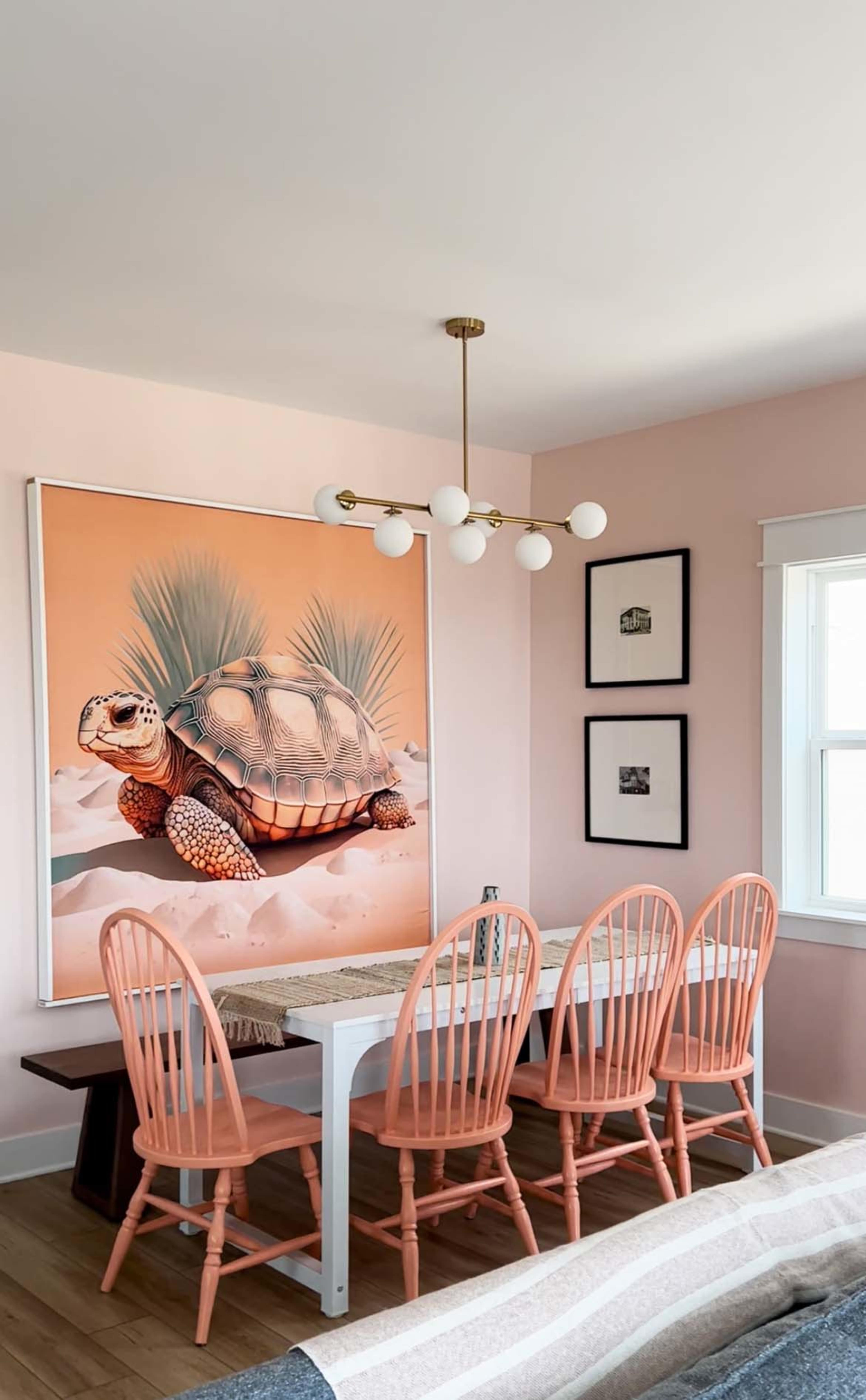 A dining area features a large turtle mural on the wall, a white table, and six pink wooden chairs arranged around it.