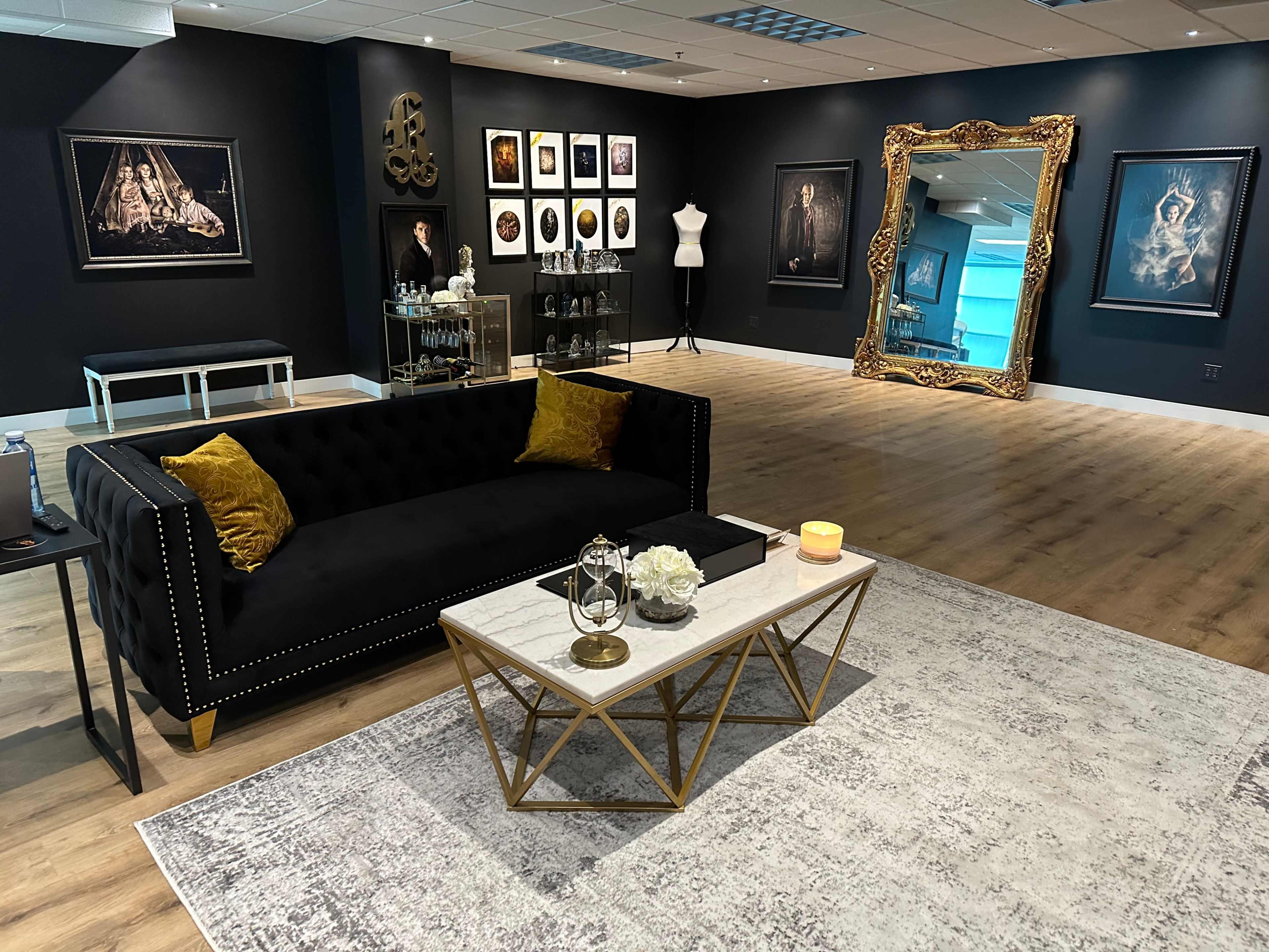 The room features a dark wall backdrop, an ornate mirror, a black sofa with yellow pillows, and various framed artworks displayed on the walls.