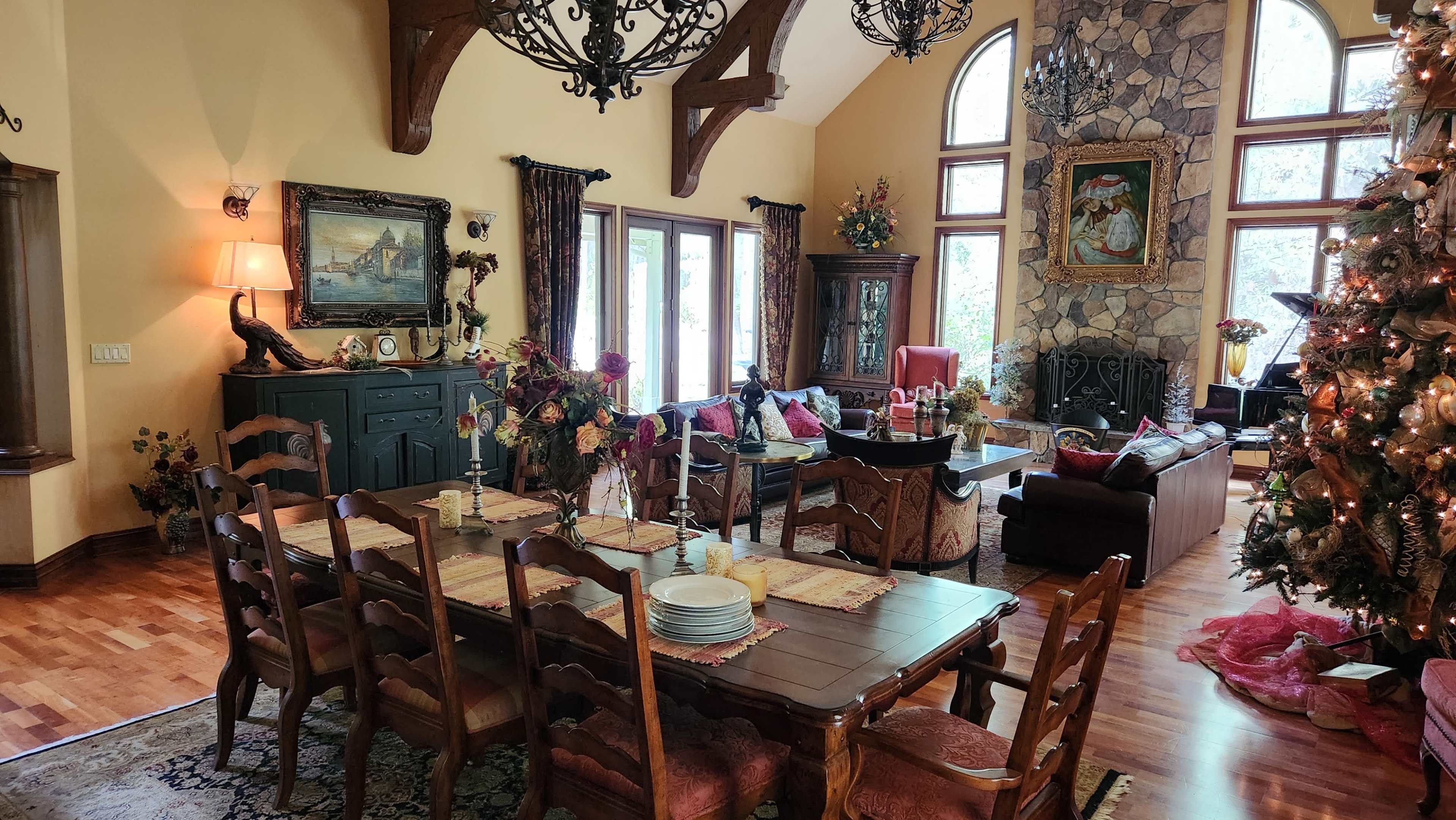 The image shows a spacious dining area with a large wooden table and chairs, adjacent to a cozy living room decorated for the holiday season.