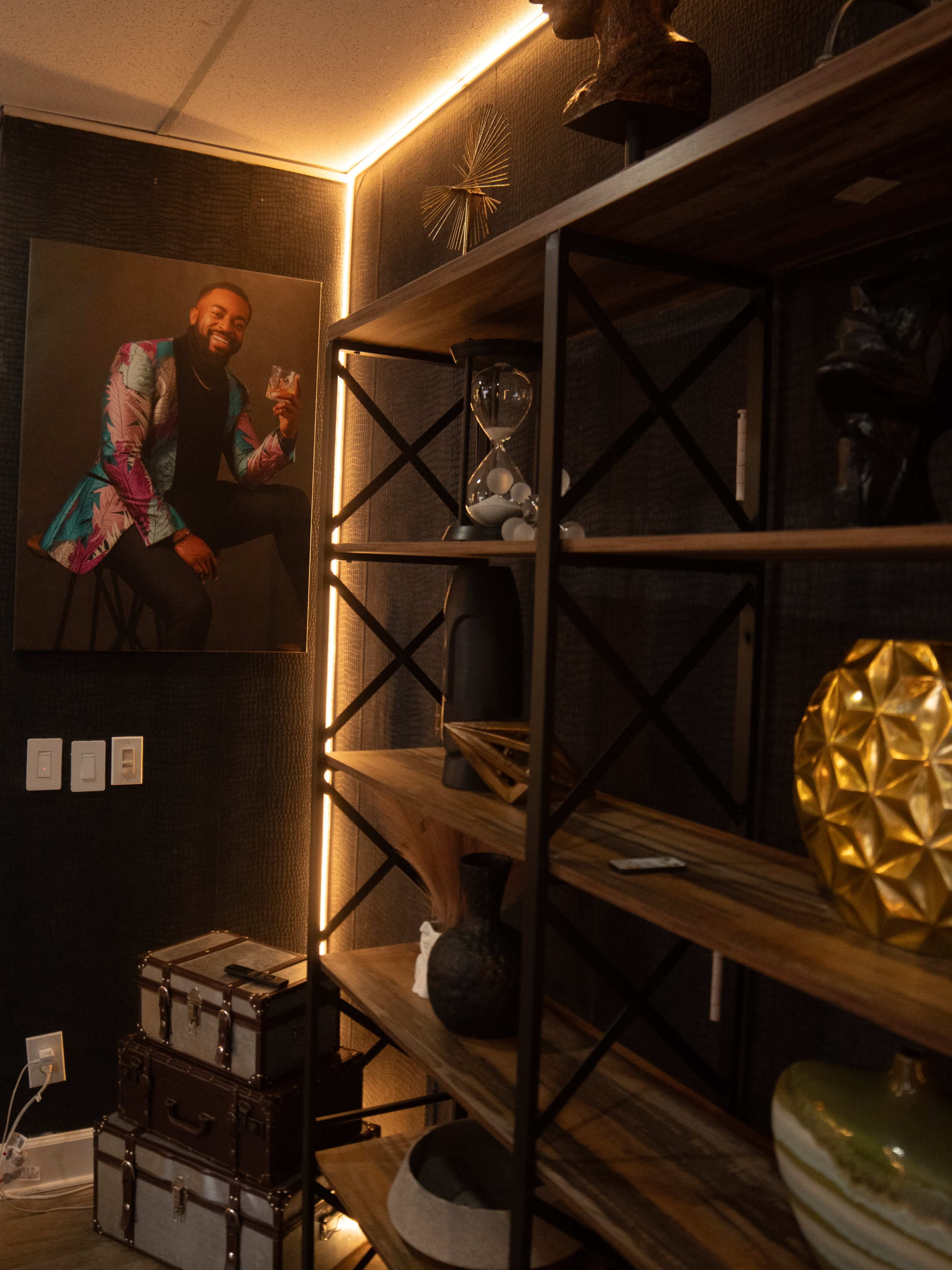 The image shows a modern interior scene featuring a shelving unit with various decorative items and a large framed portrait of a man in vibrant clothing on the wall.