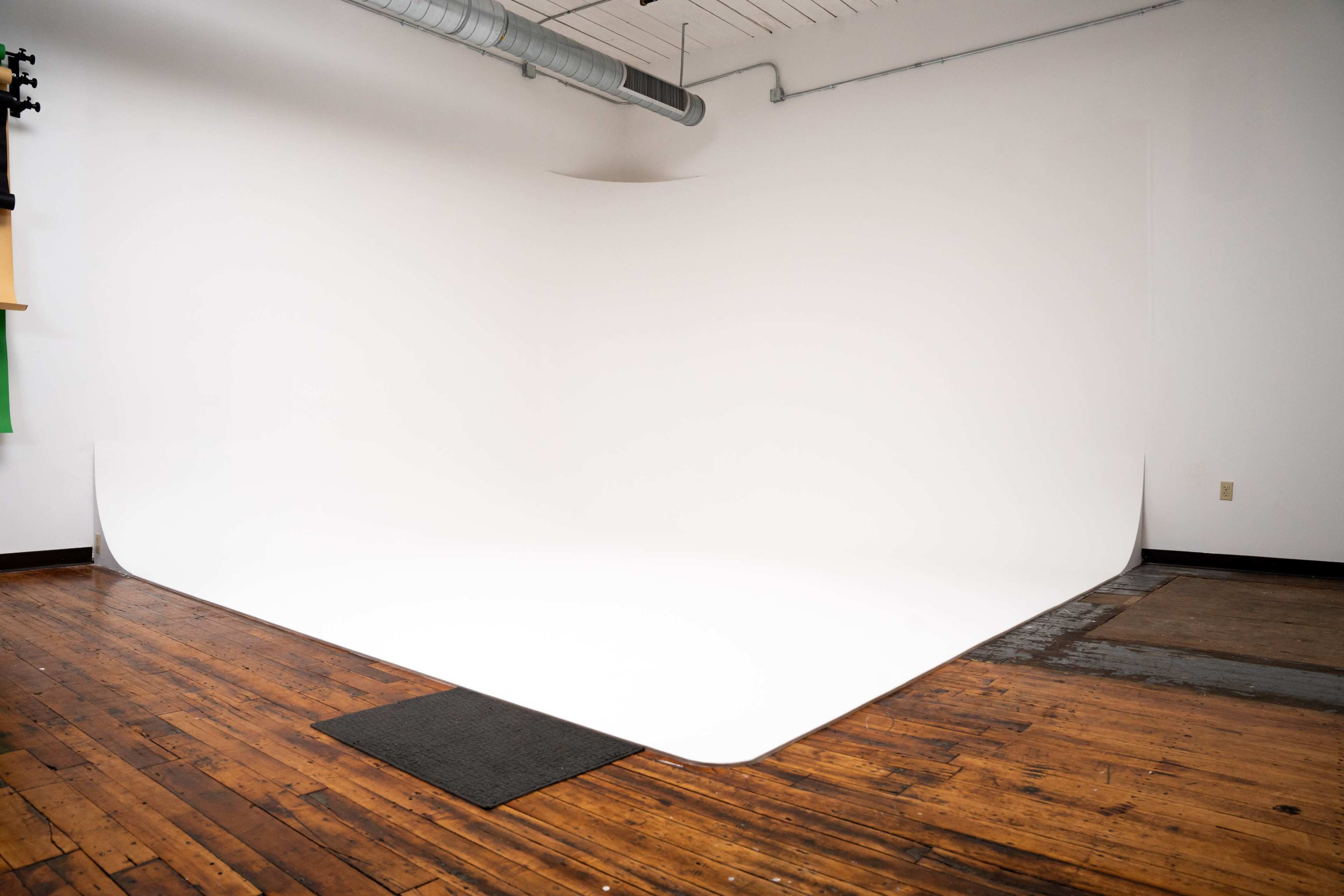 A clean, white photo studio backdrop on wooden flooring.