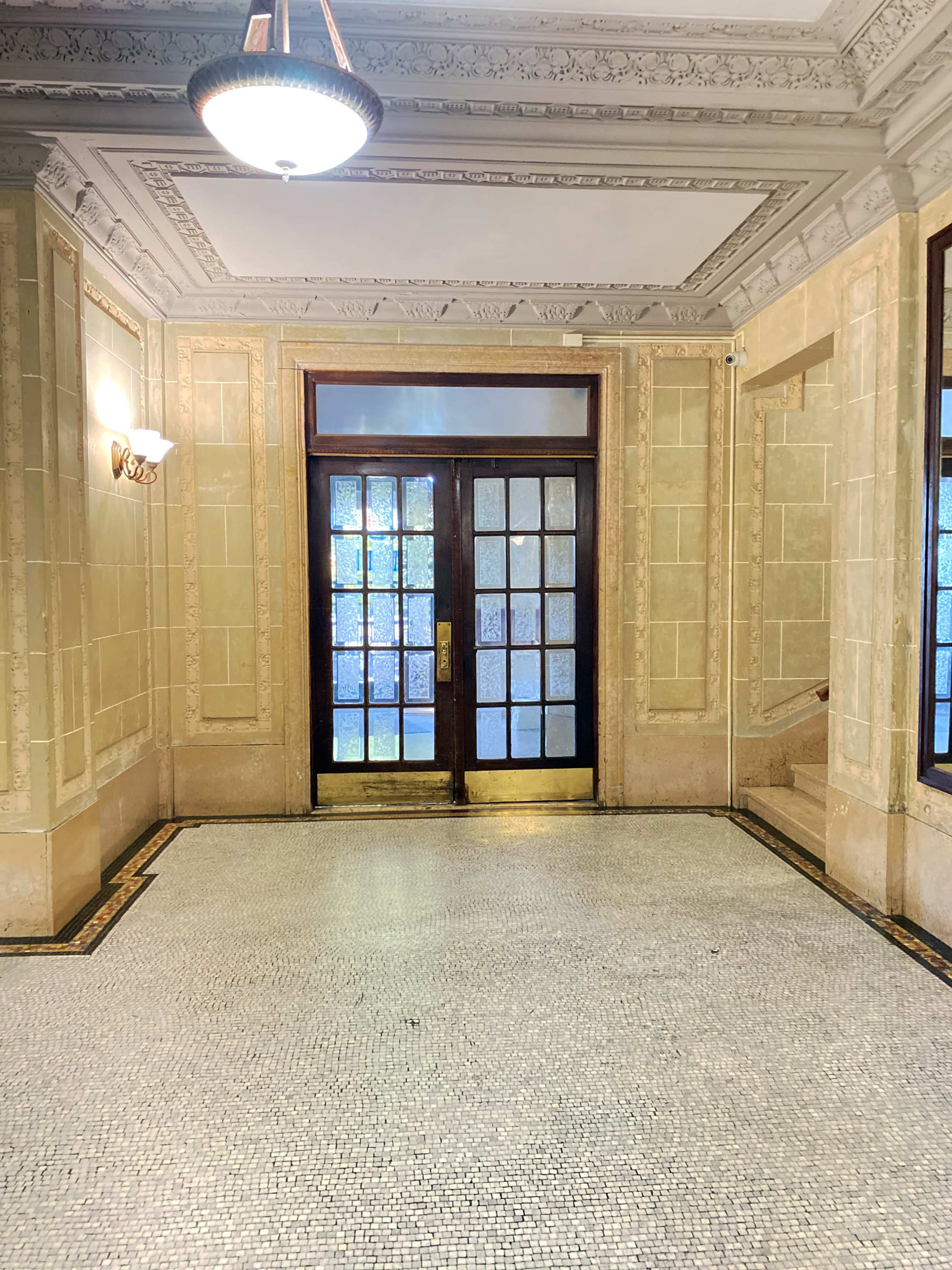 The image shows a lobby area with ornate walls, double doors featuring glass panels, and a mosaic tile floor.