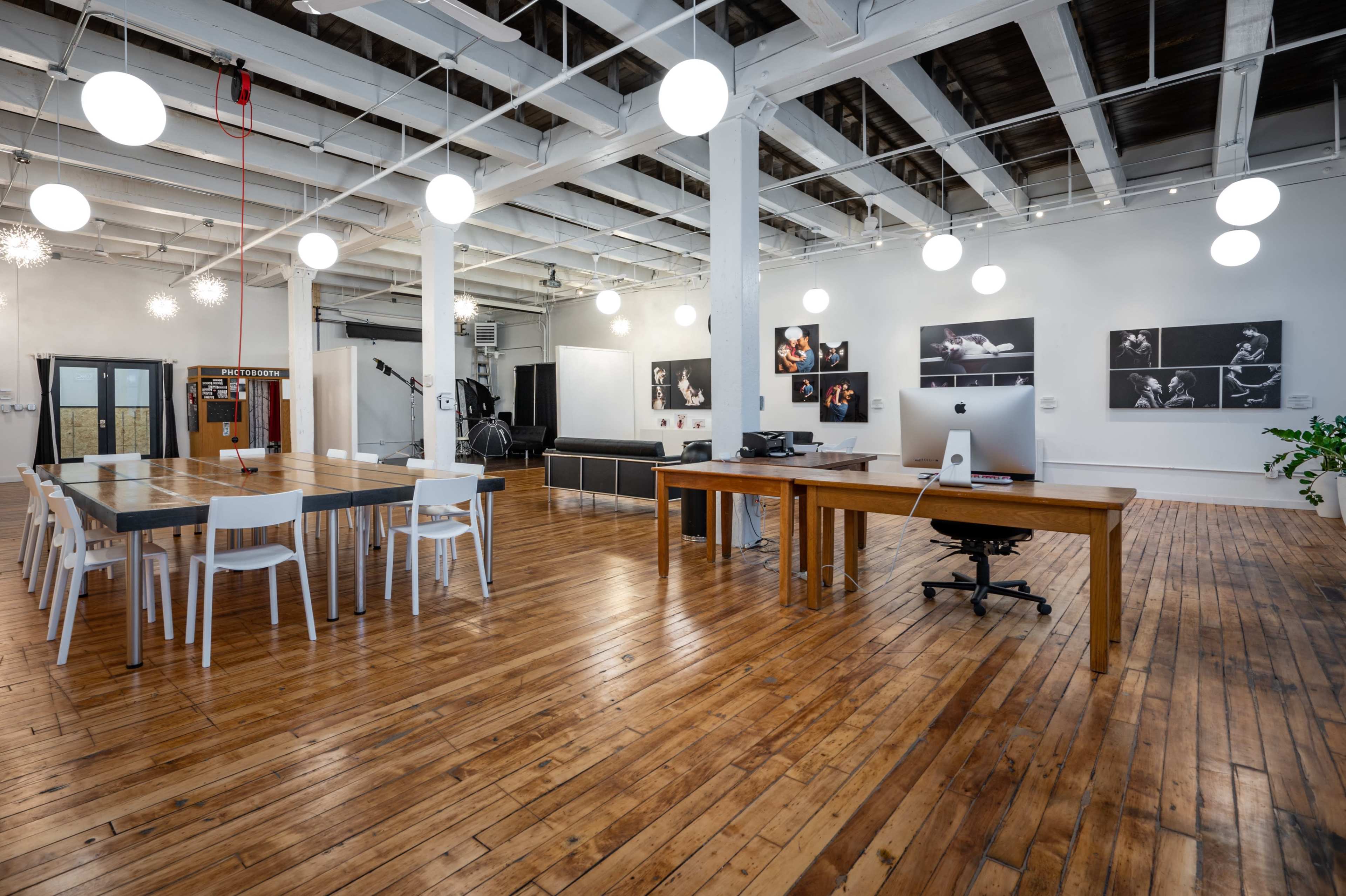 The image shows a spacious office area with wooden flooring, a large table with white chairs, and photographic displays on the walls.