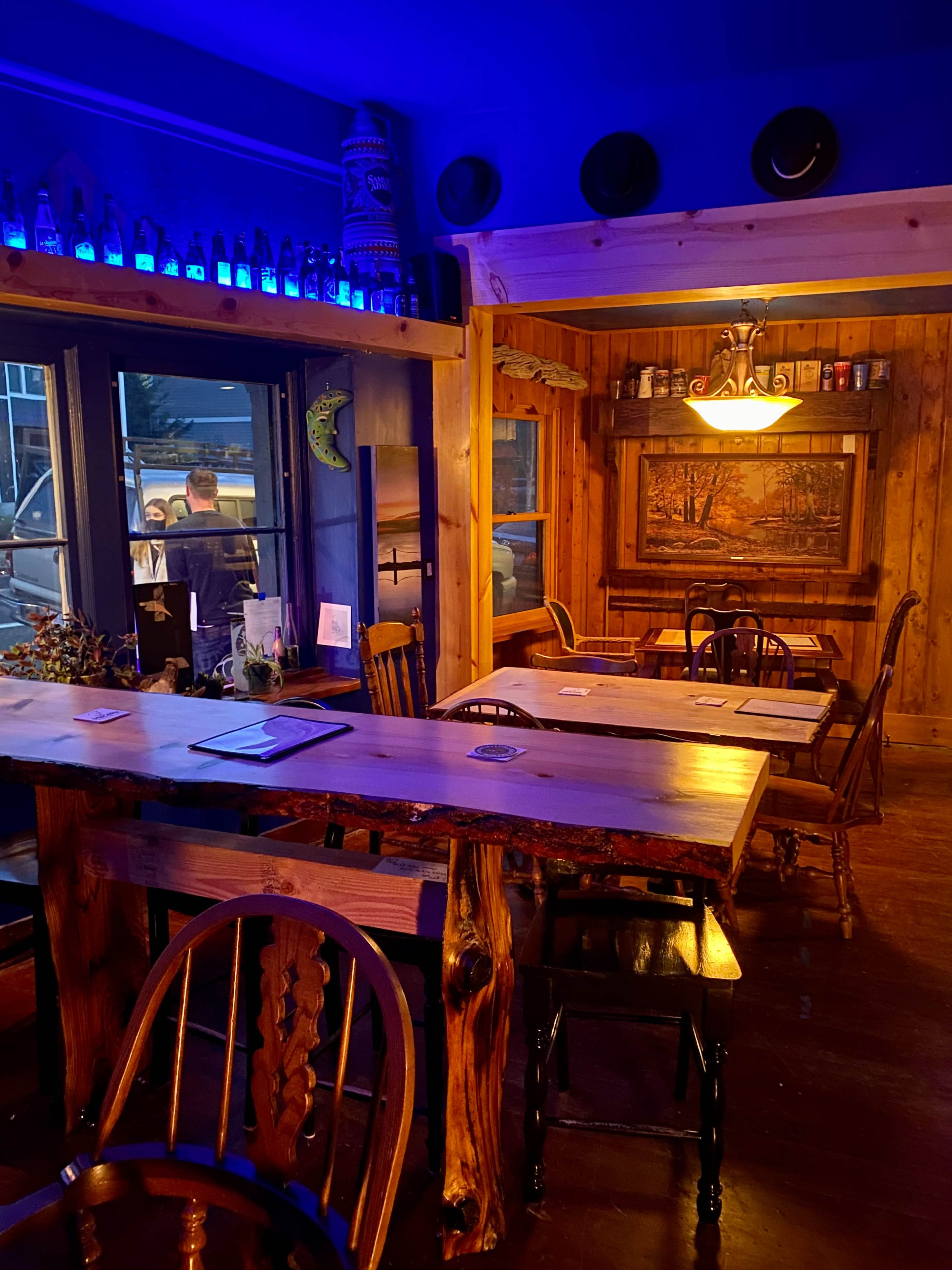 A rustic interior of a restaurant with wooden tables, chairs, and blue ambient lighting.