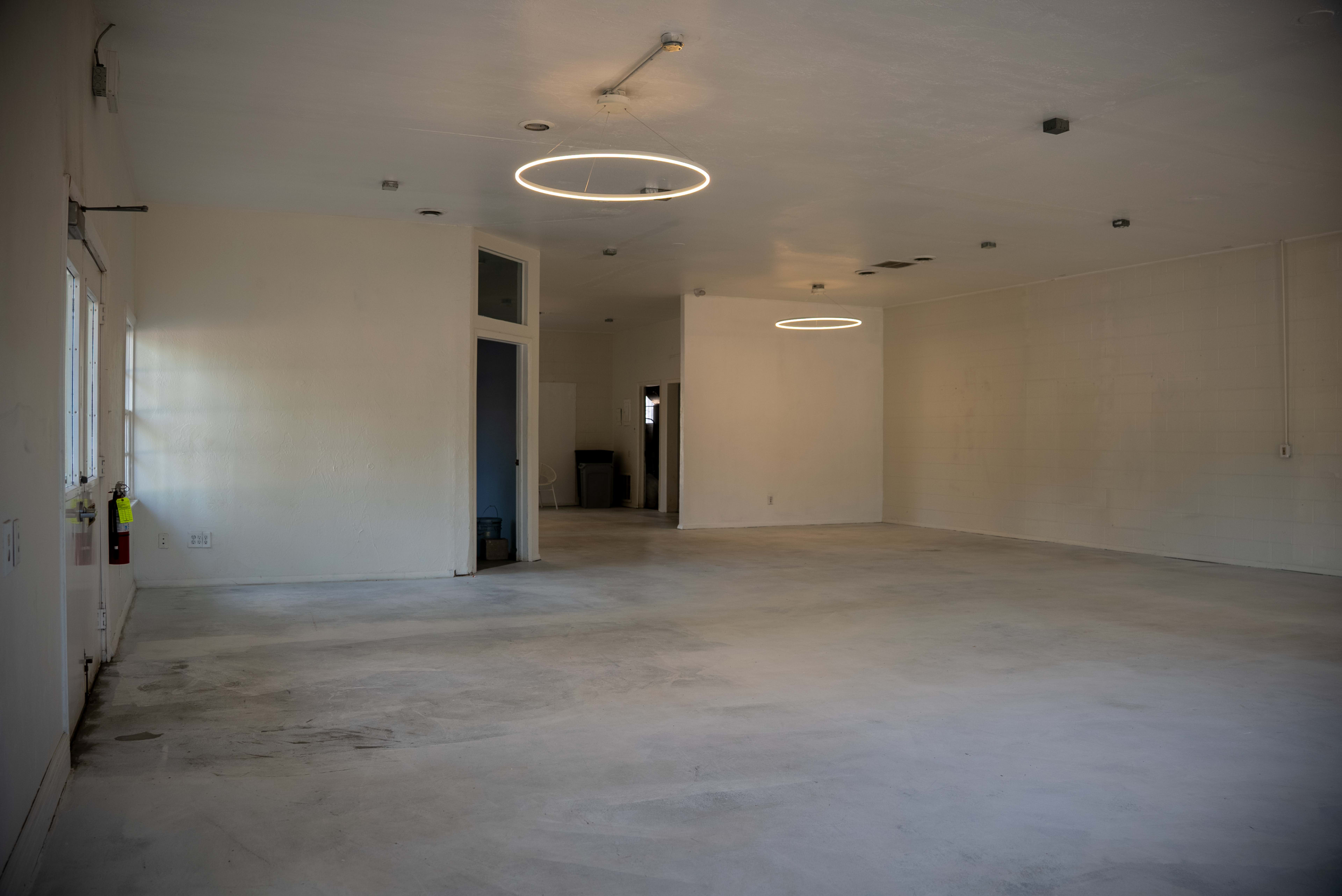 The image shows a spacious, empty room with two circular light fixtures hanging from the ceiling and doors leading to other areas.