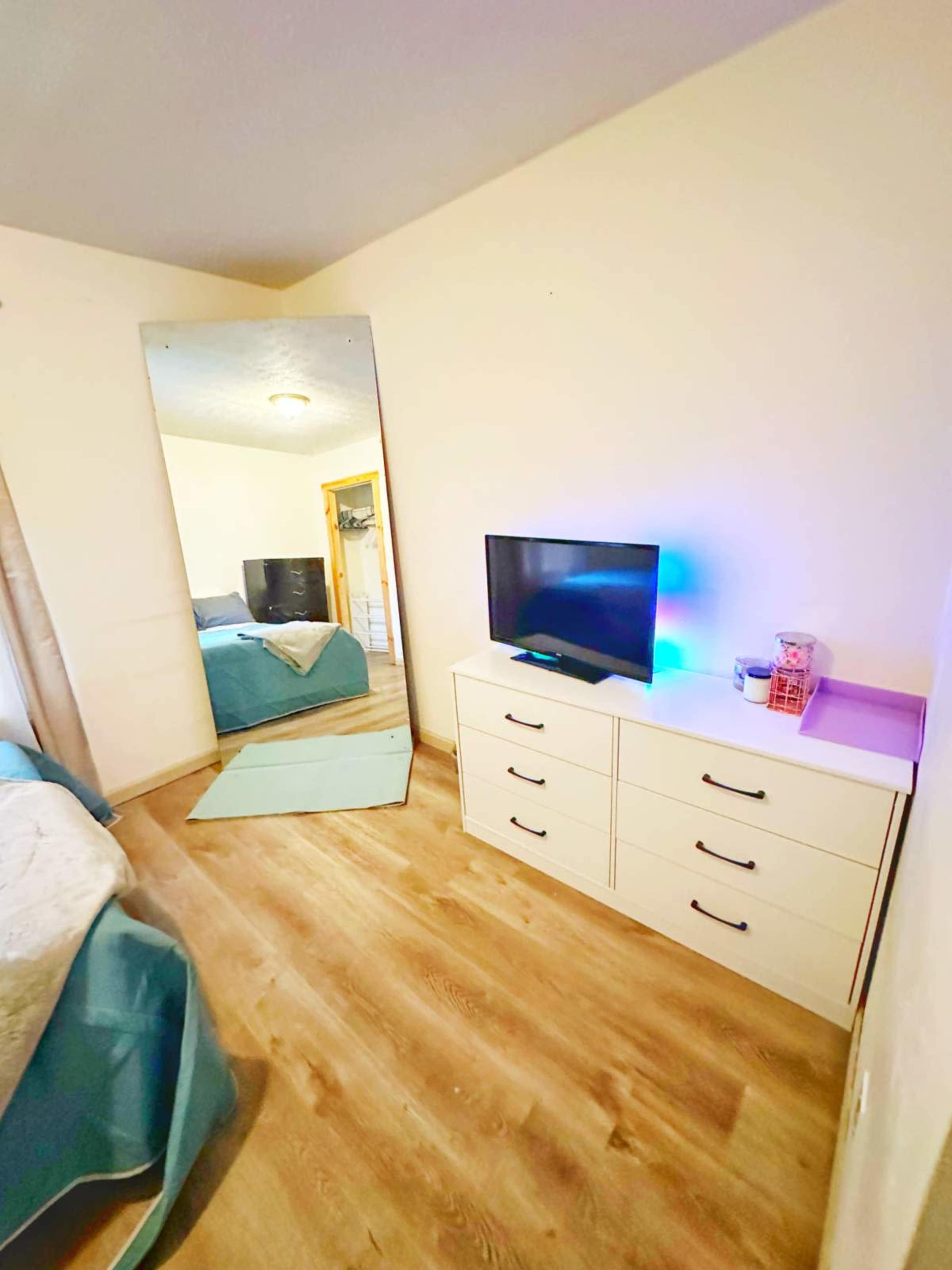 A bedroom with a television on a dresser, a large mirror, and a bed with light blue bedding.
