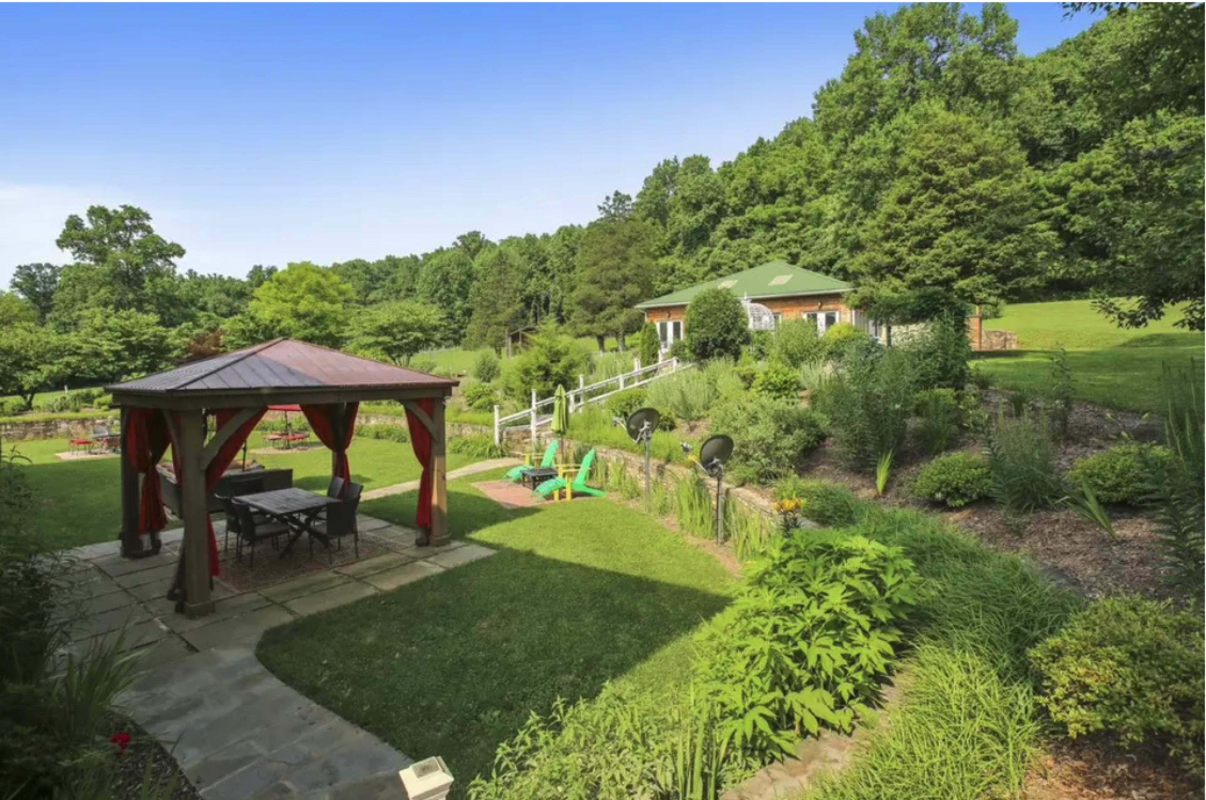 A landscaped garden with a gazebo, outdoor seating, and a house surrounded by greenery.