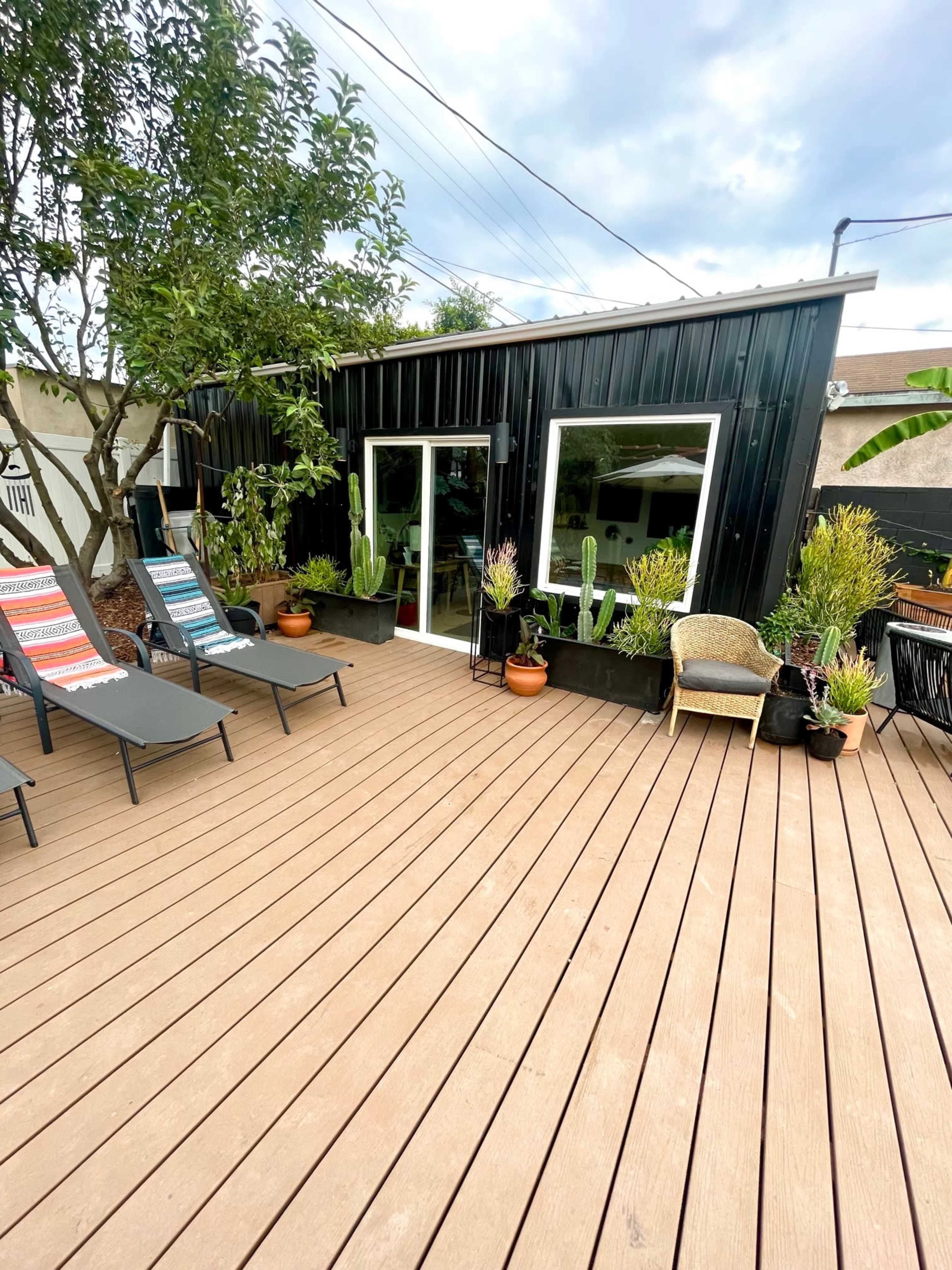 A wooden deck with two lounge chairs and potted plants in front of a modern black building featuring large windows.