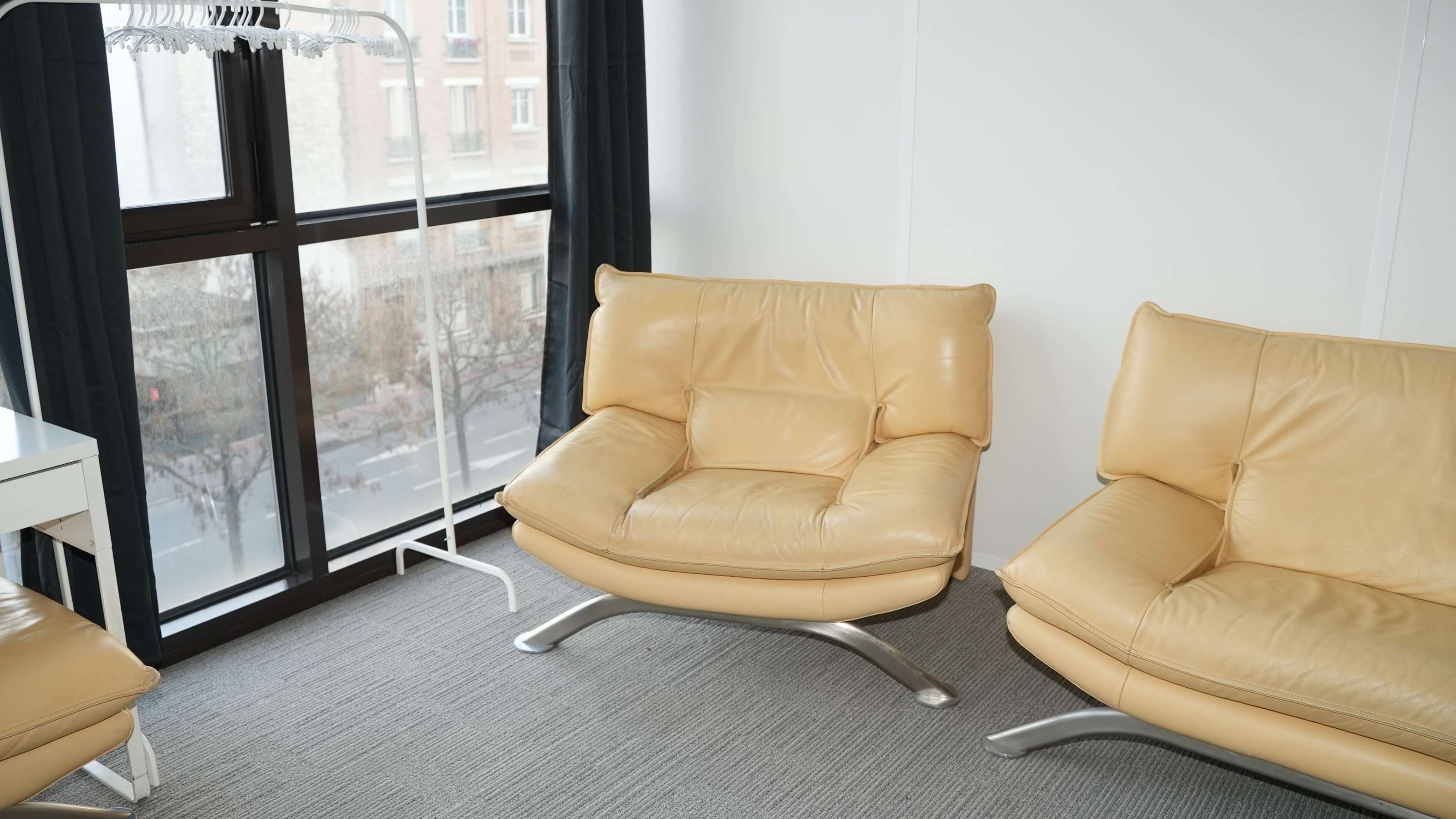 The image shows a corner of a room featuring two cream-colored leather chairs with sleek metal bases positioned near a large window.