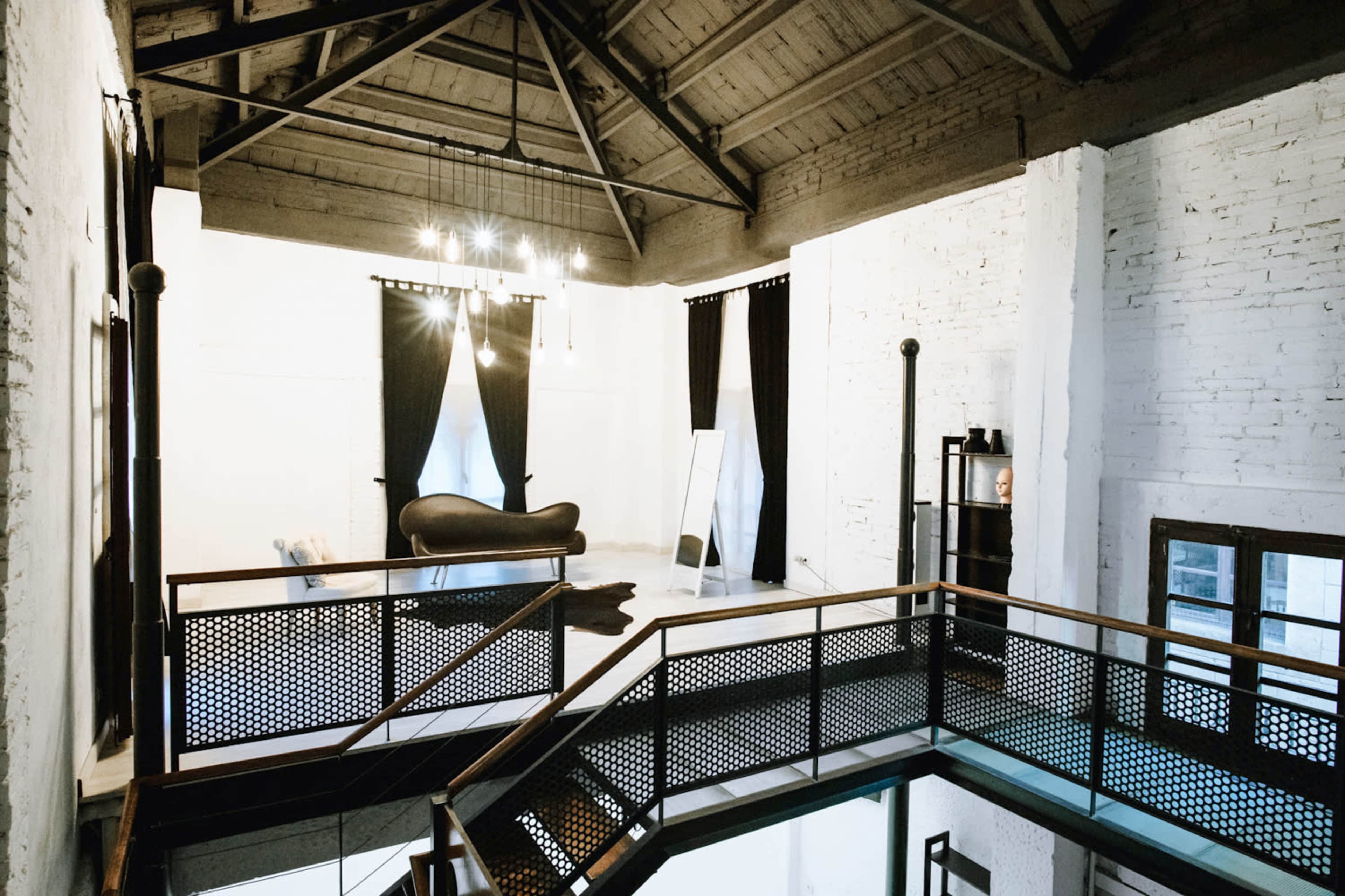A spacious interior with high ceilings, featuring a lofted area overlooking a seating space with a mirror and black curtains.