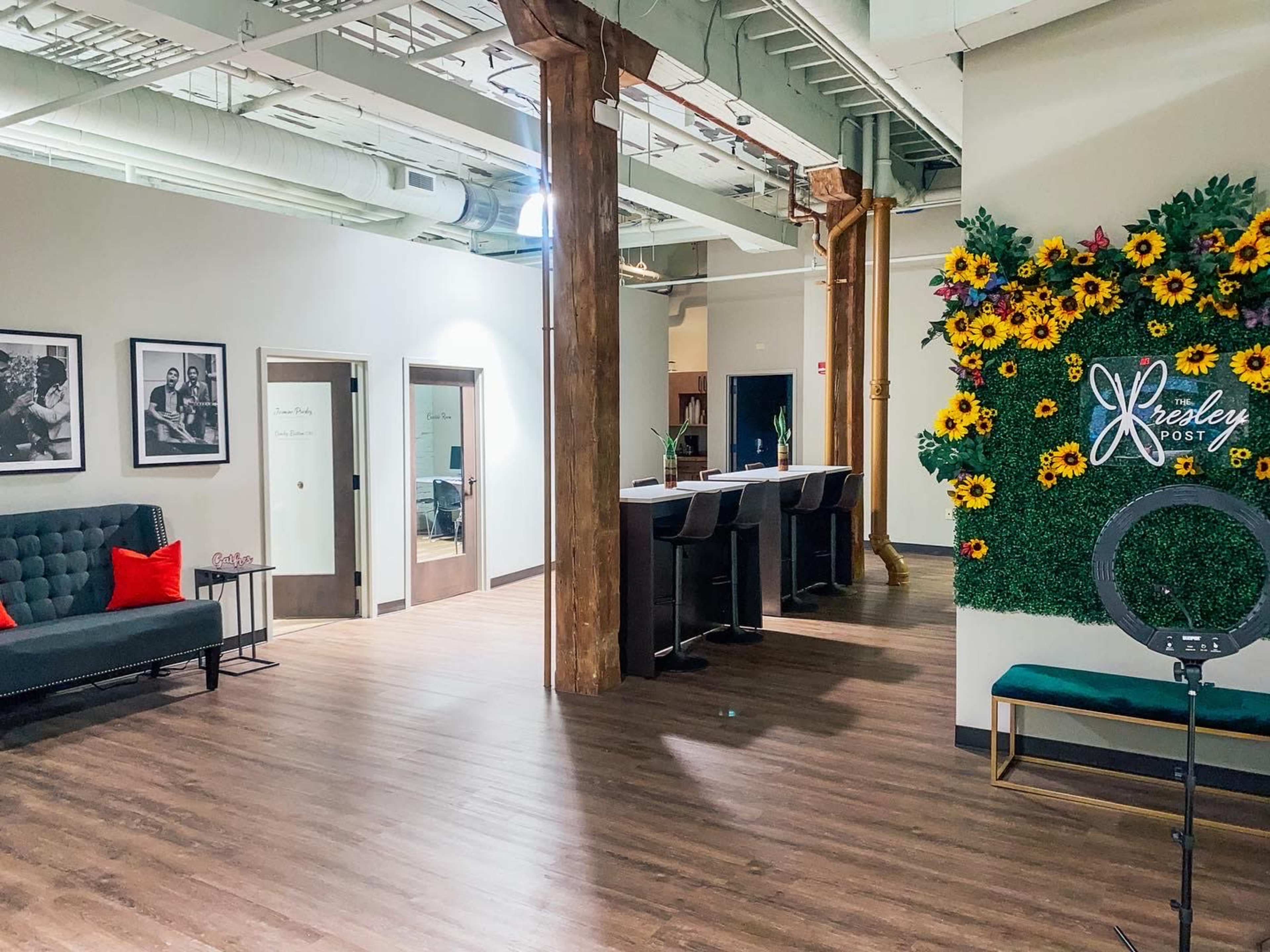 A modern office interior with a seating area, a bar-style counter, and a decorative wall featuring sunflowers.