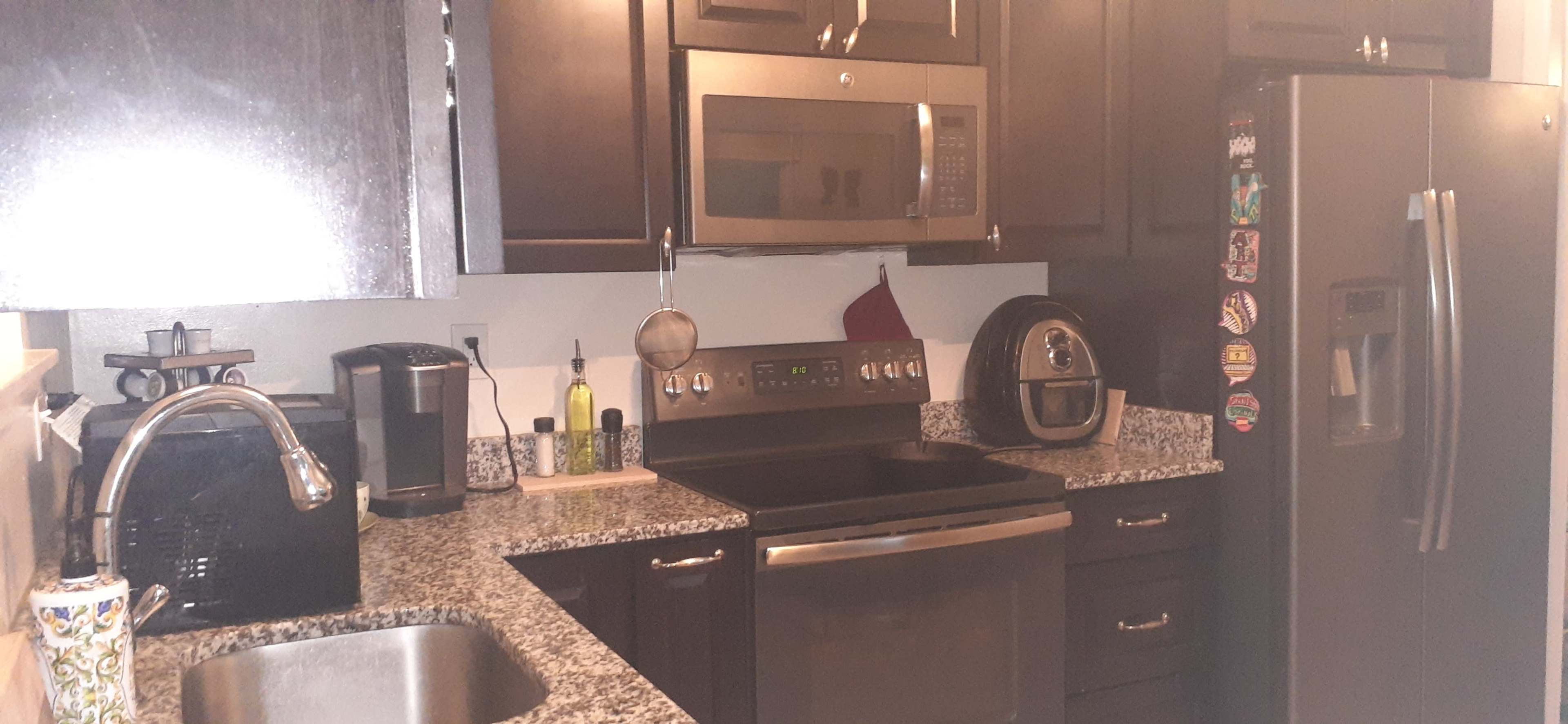 The kitchen features dark cabinets, stainless steel appliances, and a countertop with a sink and various kitchen tools.