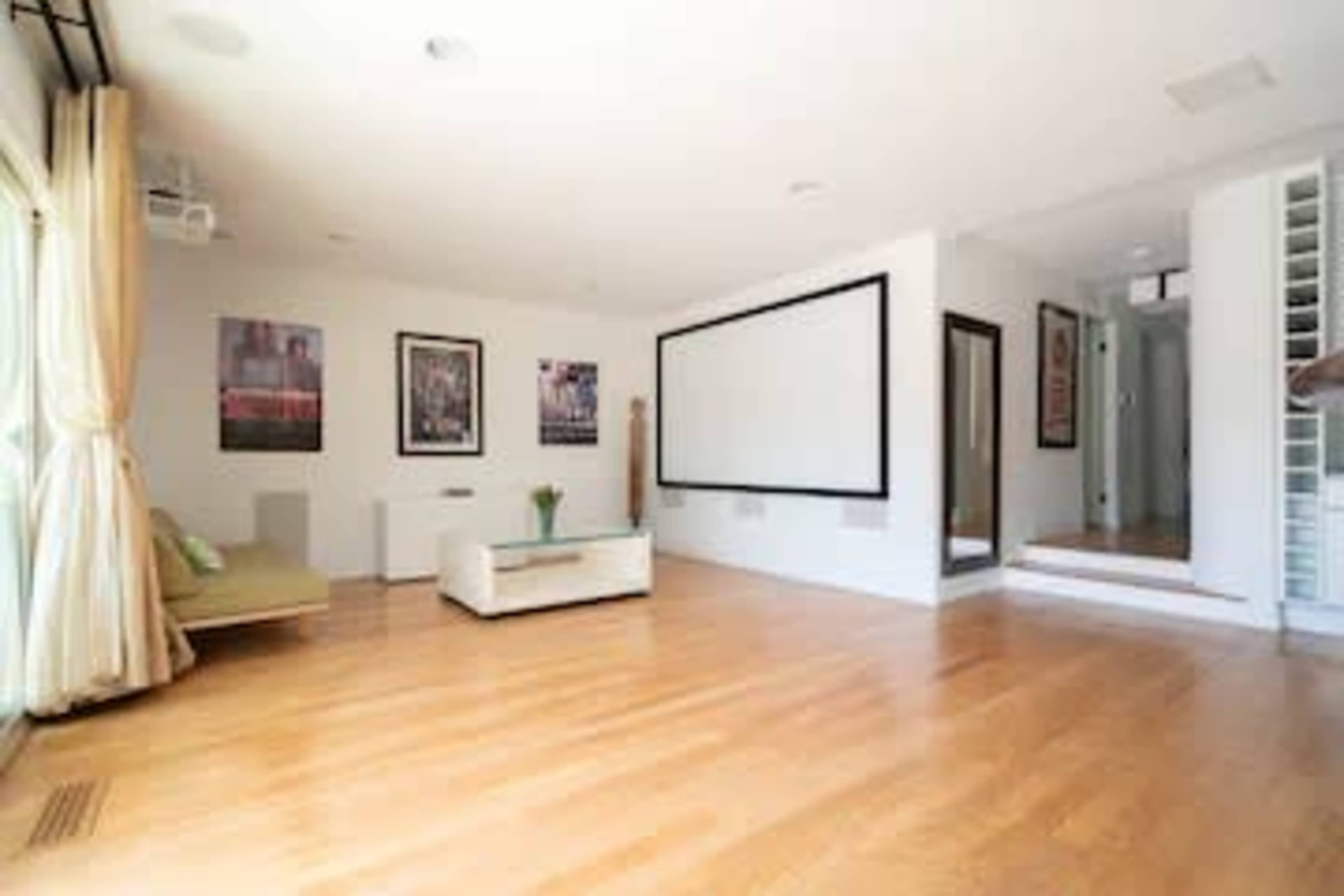 A modern living room features hardwood flooring, a large screen on the wall, and framed artwork.