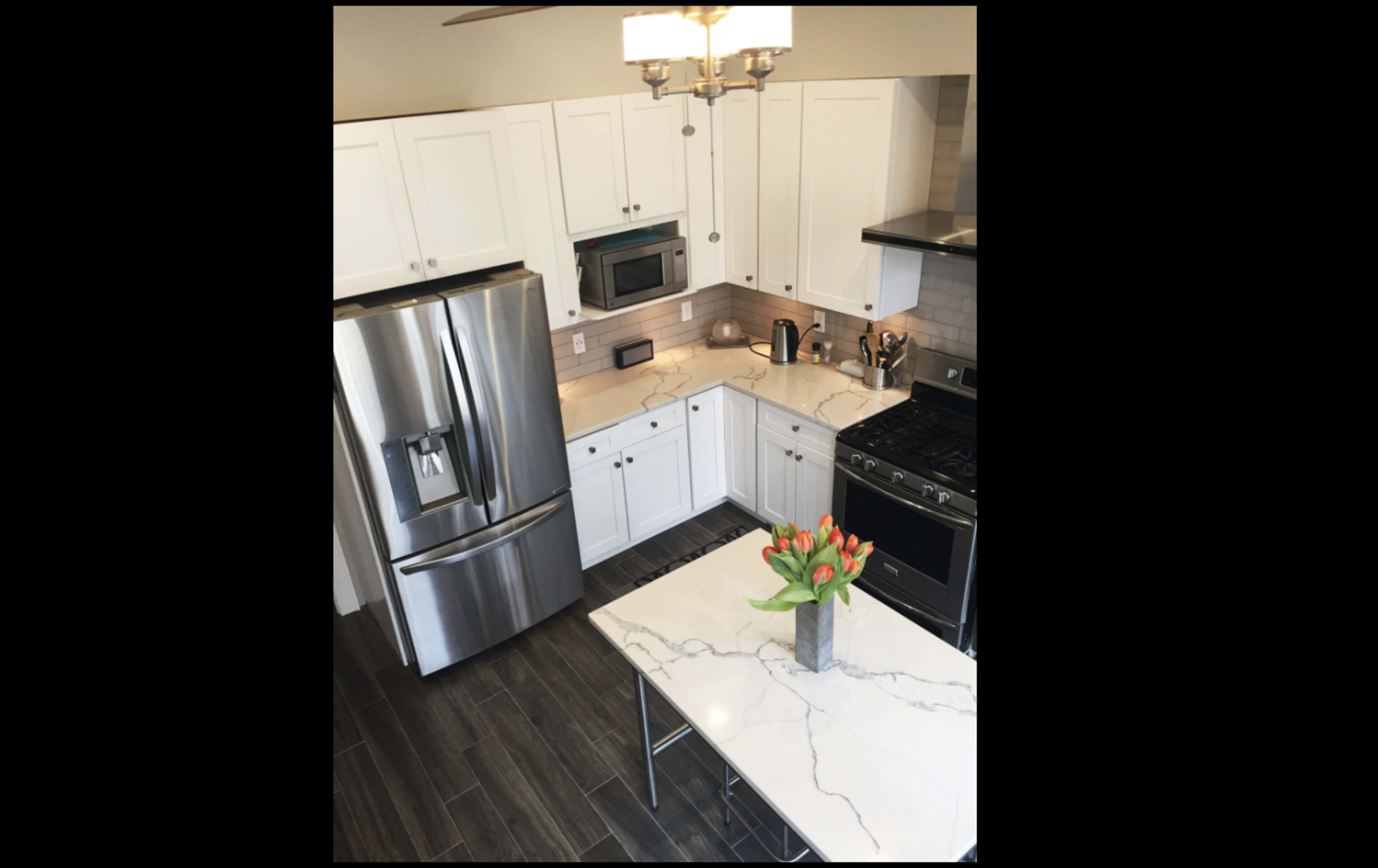 A modern kitchen features stainless steel appliances, white cabinets, and a marble-topped island with a vase of tulips.