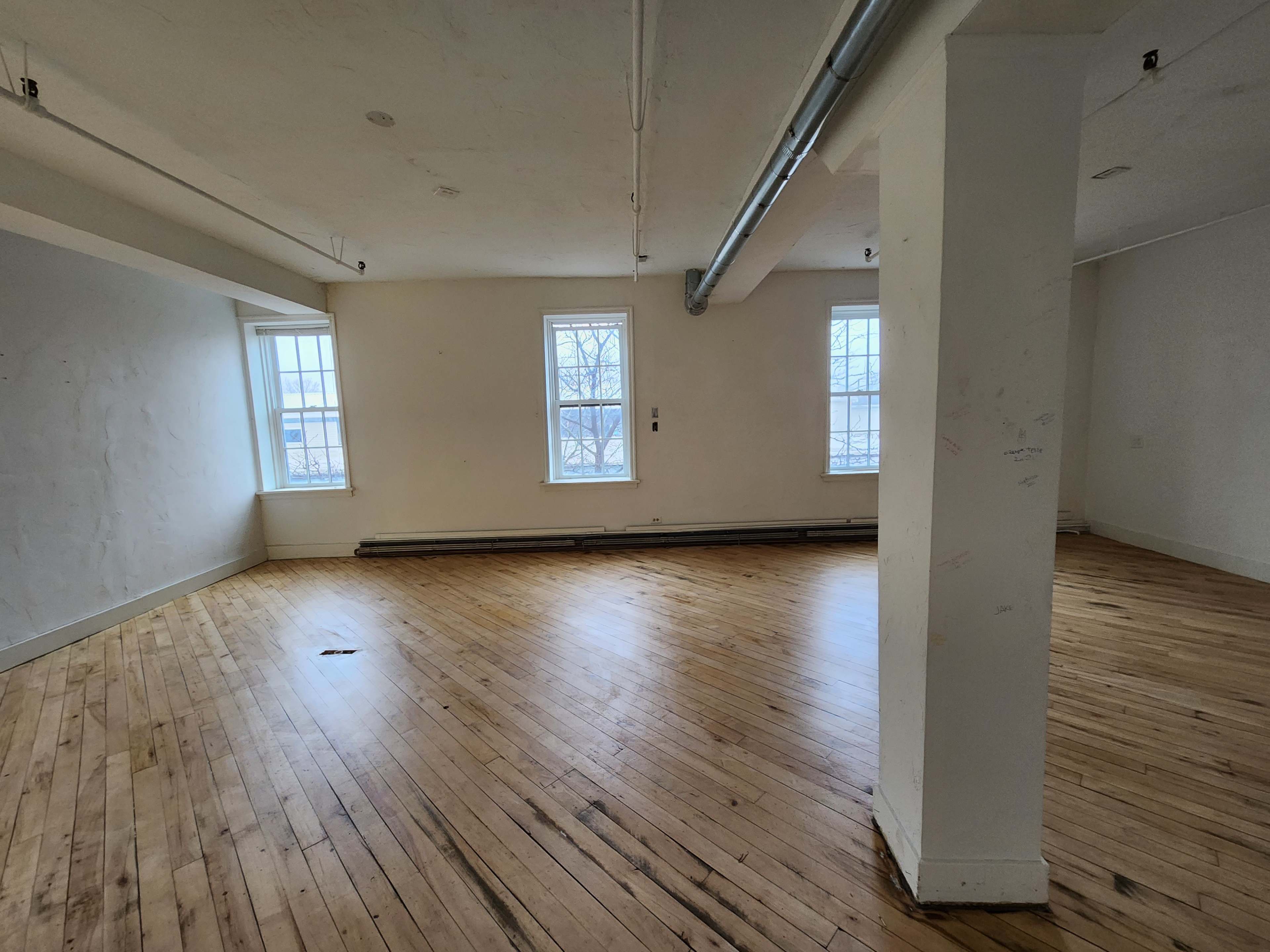 An empty room with wooden floors, white walls, and two windows on one side.
