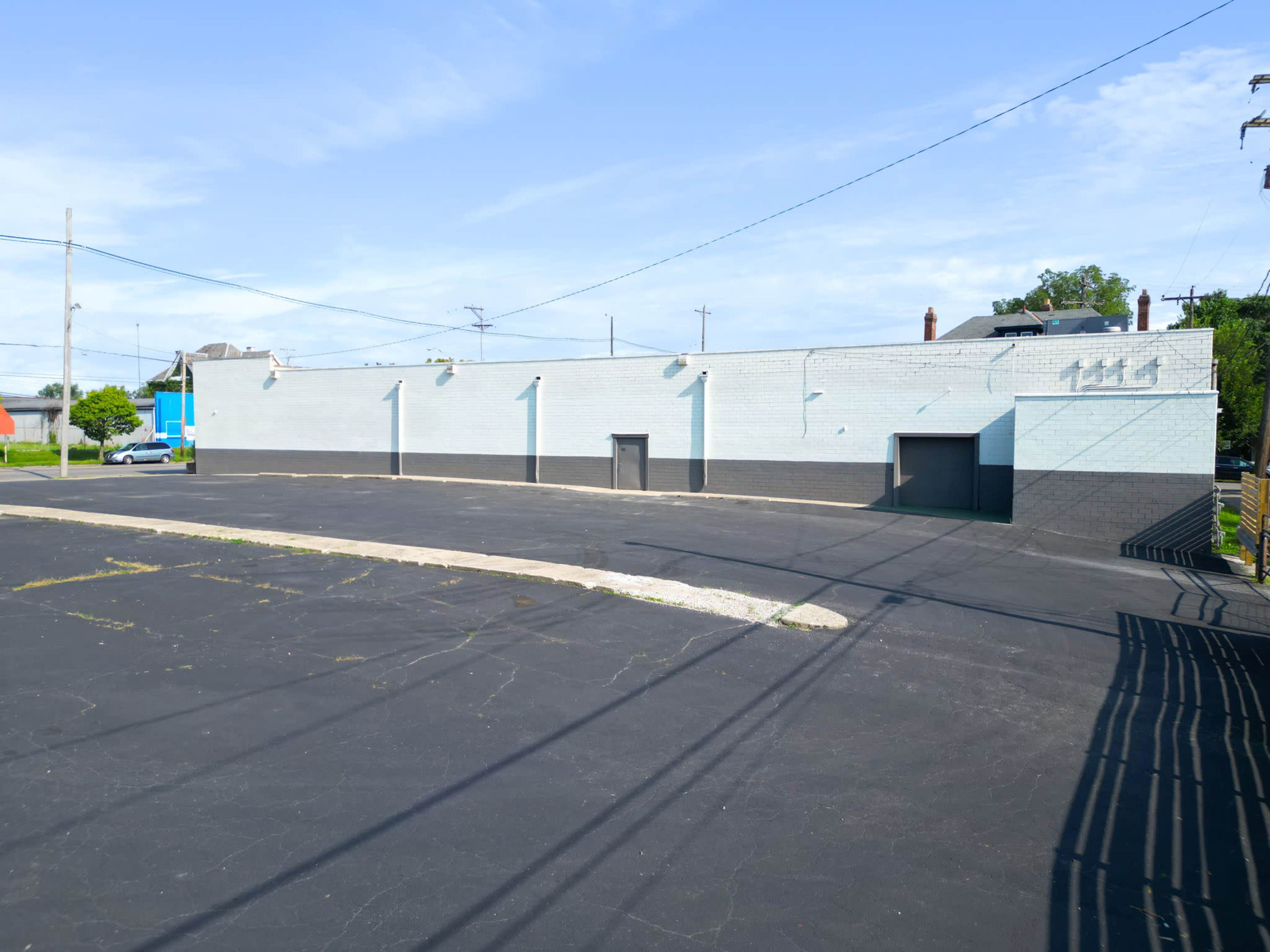 A vacant commercial building with a large asphalt parking lot and utility poles in the background.