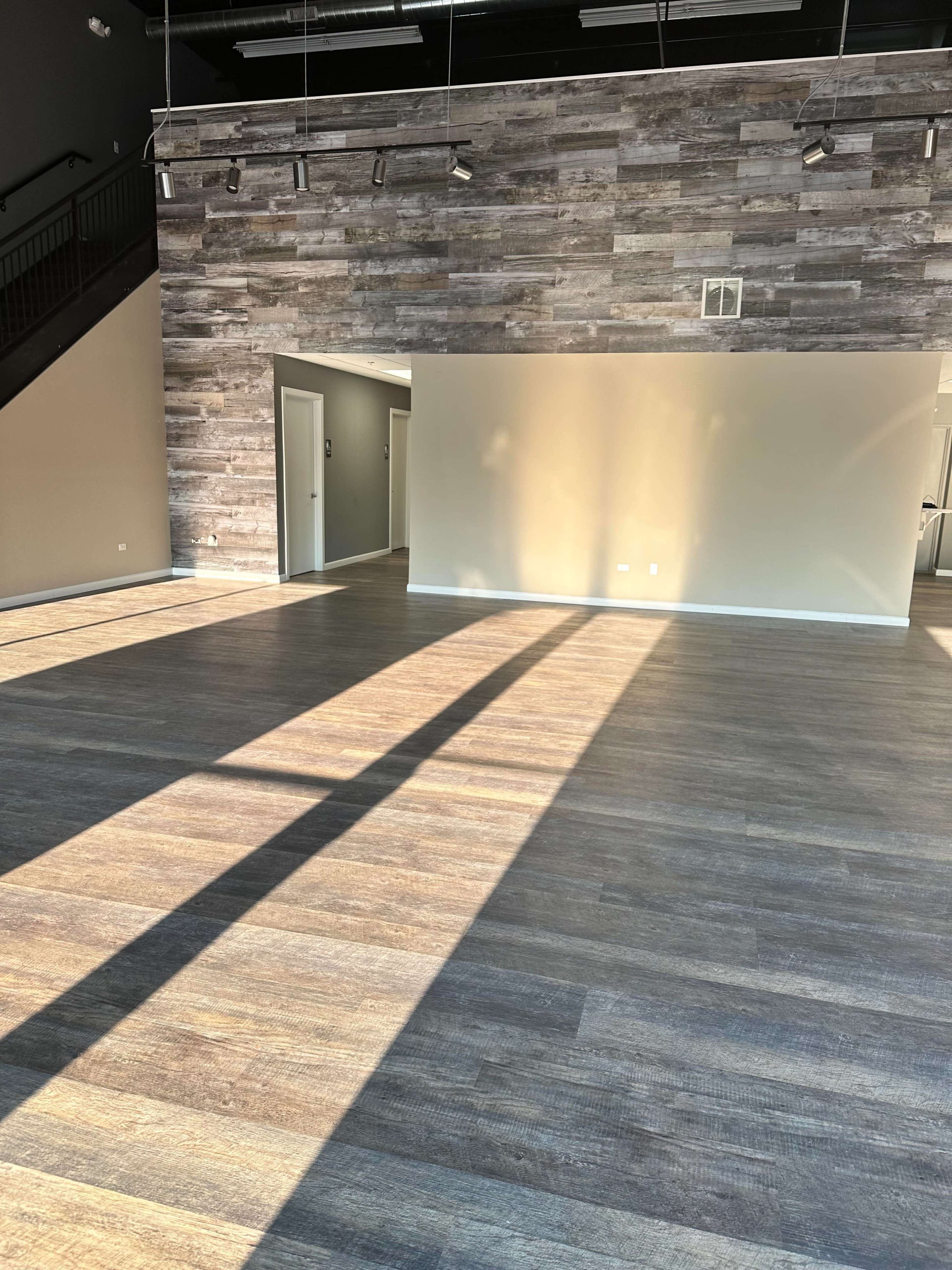 The image shows a spacious interior with wooden flooring, a textured wall, and natural light casting long shadows across the room.