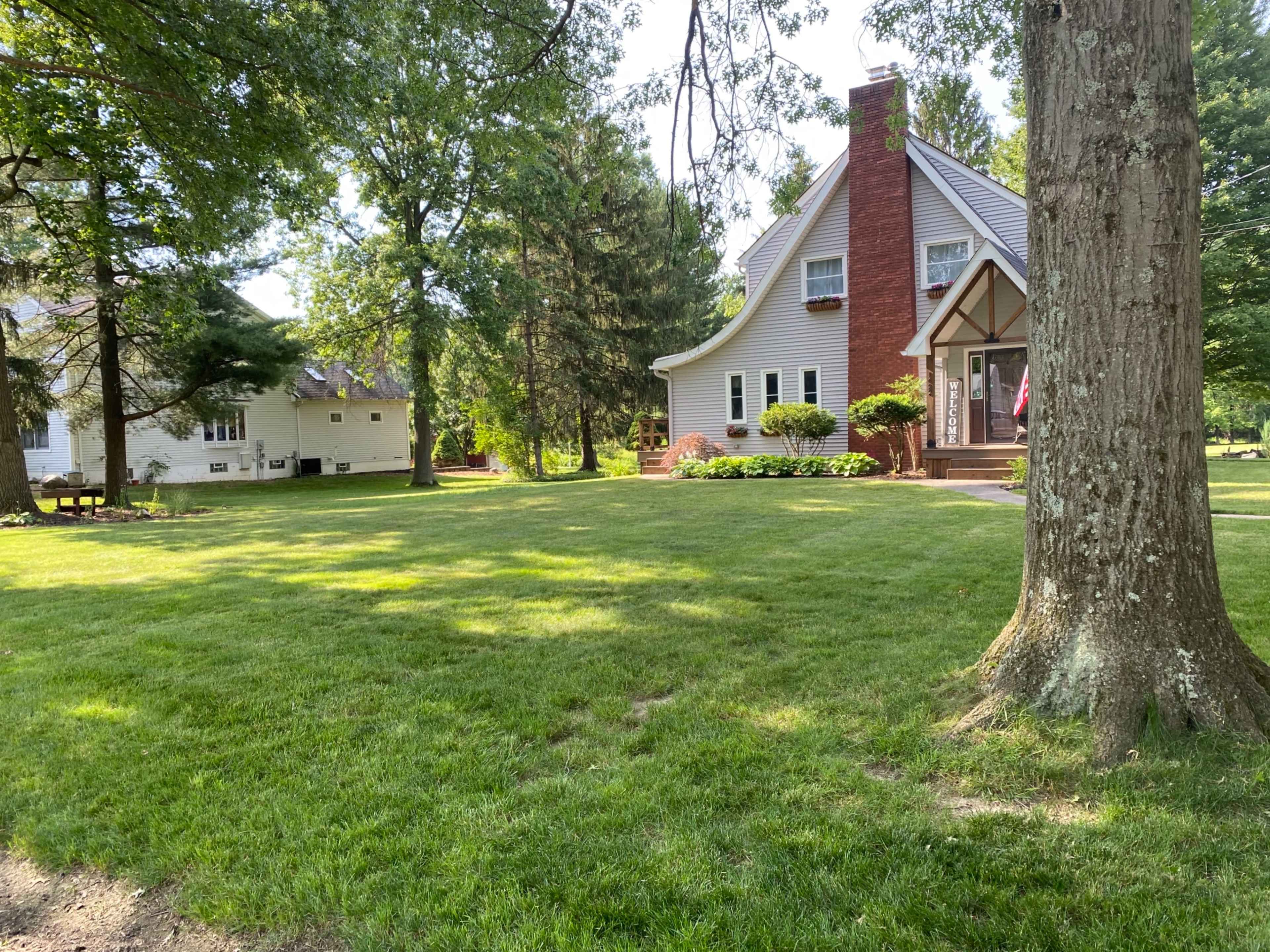 A well-maintained house with a peaked roof and a red brick chimney, set in a grassy yard surrounded by trees.