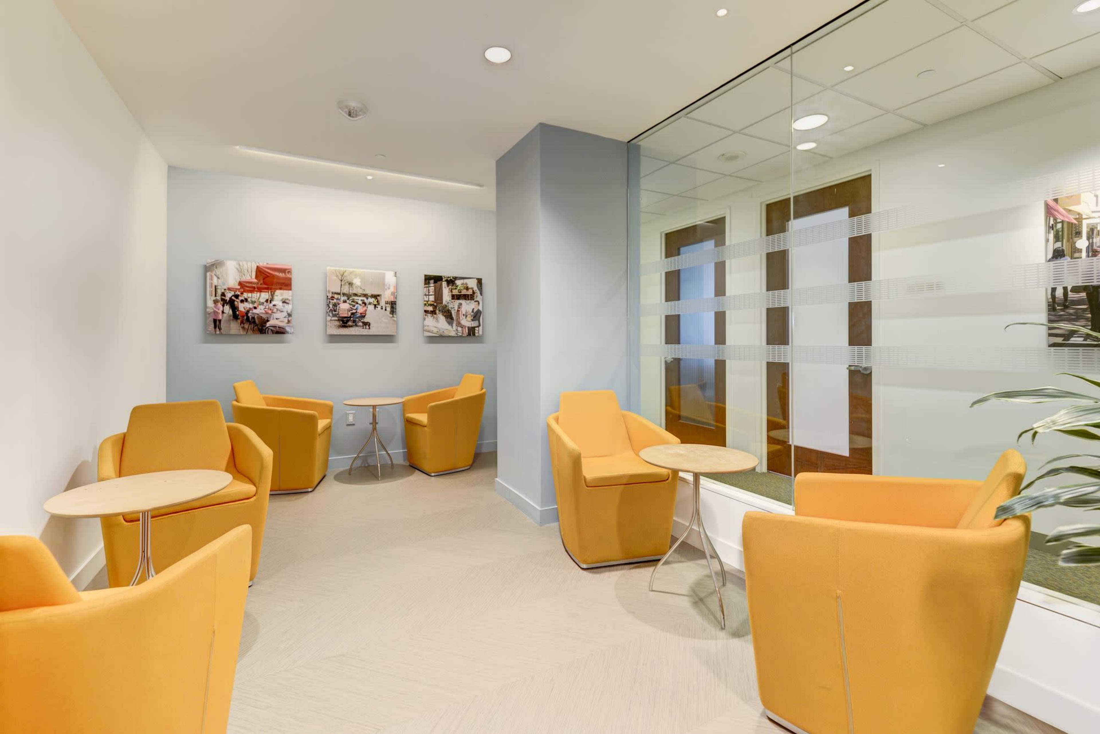 A small lounge area with orange chairs, round tables, and framed pictures on the wall.