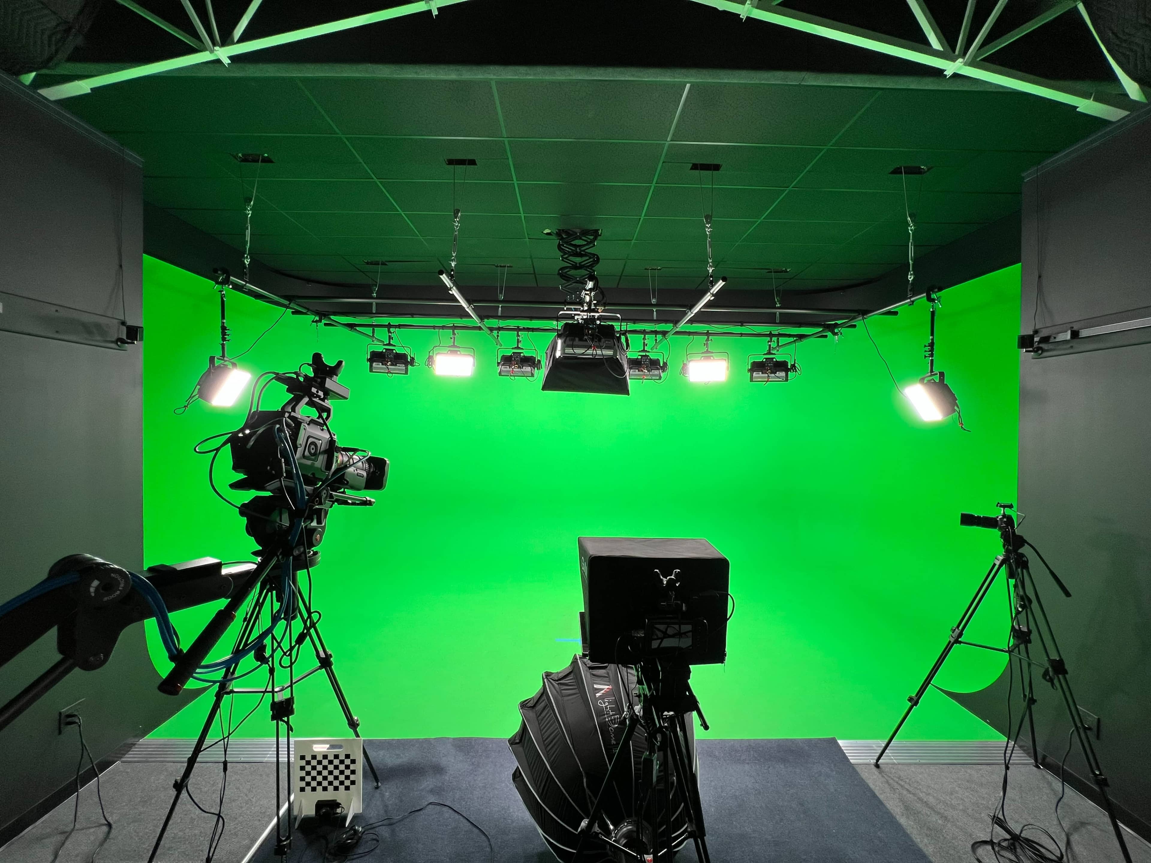 A green screen studio setup with multiple cameras and overhead lights arranged around a clean, bright green backdrop.