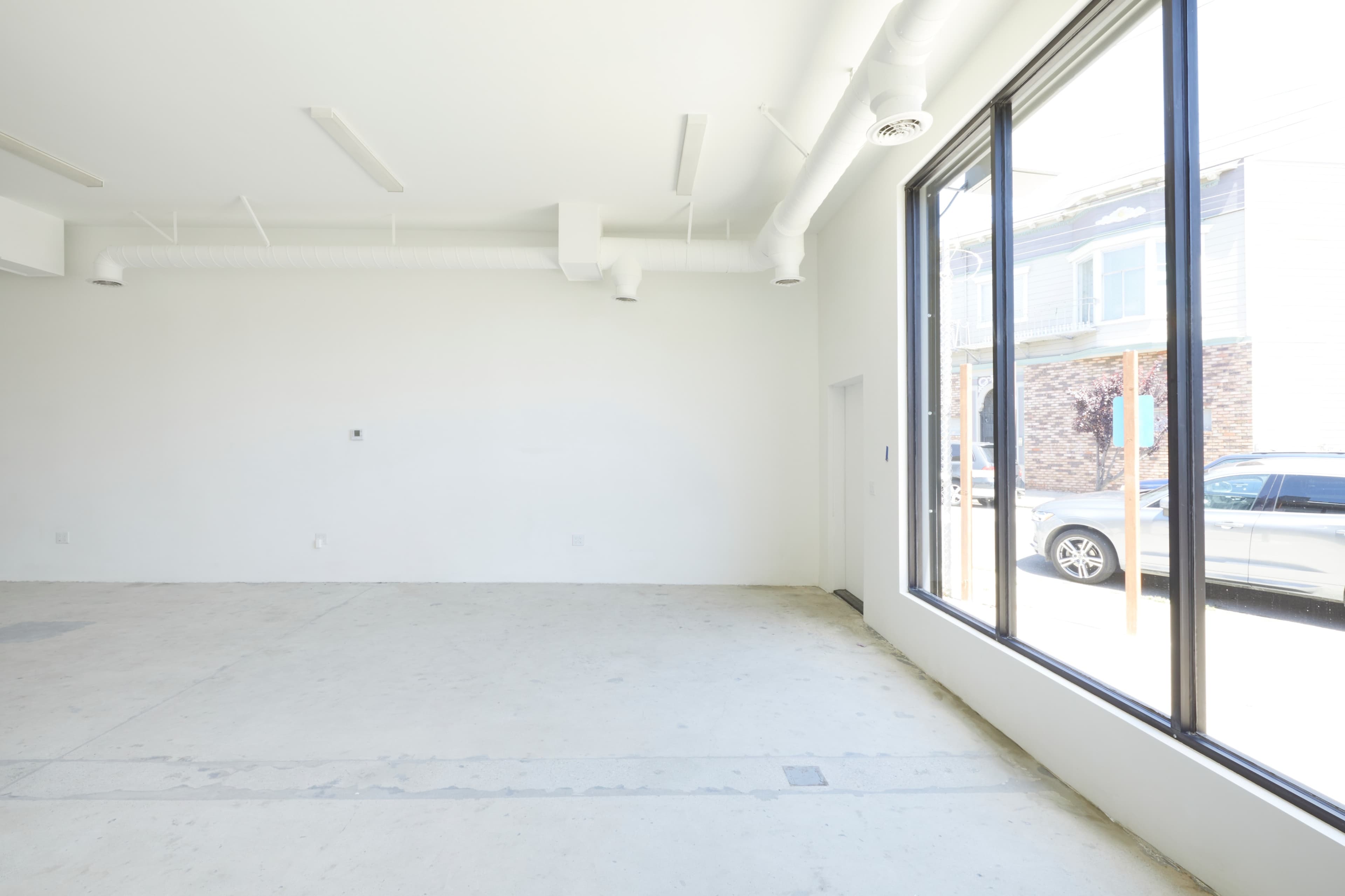 A spacious, empty interior with white walls and large windows allowing natural light to enter.