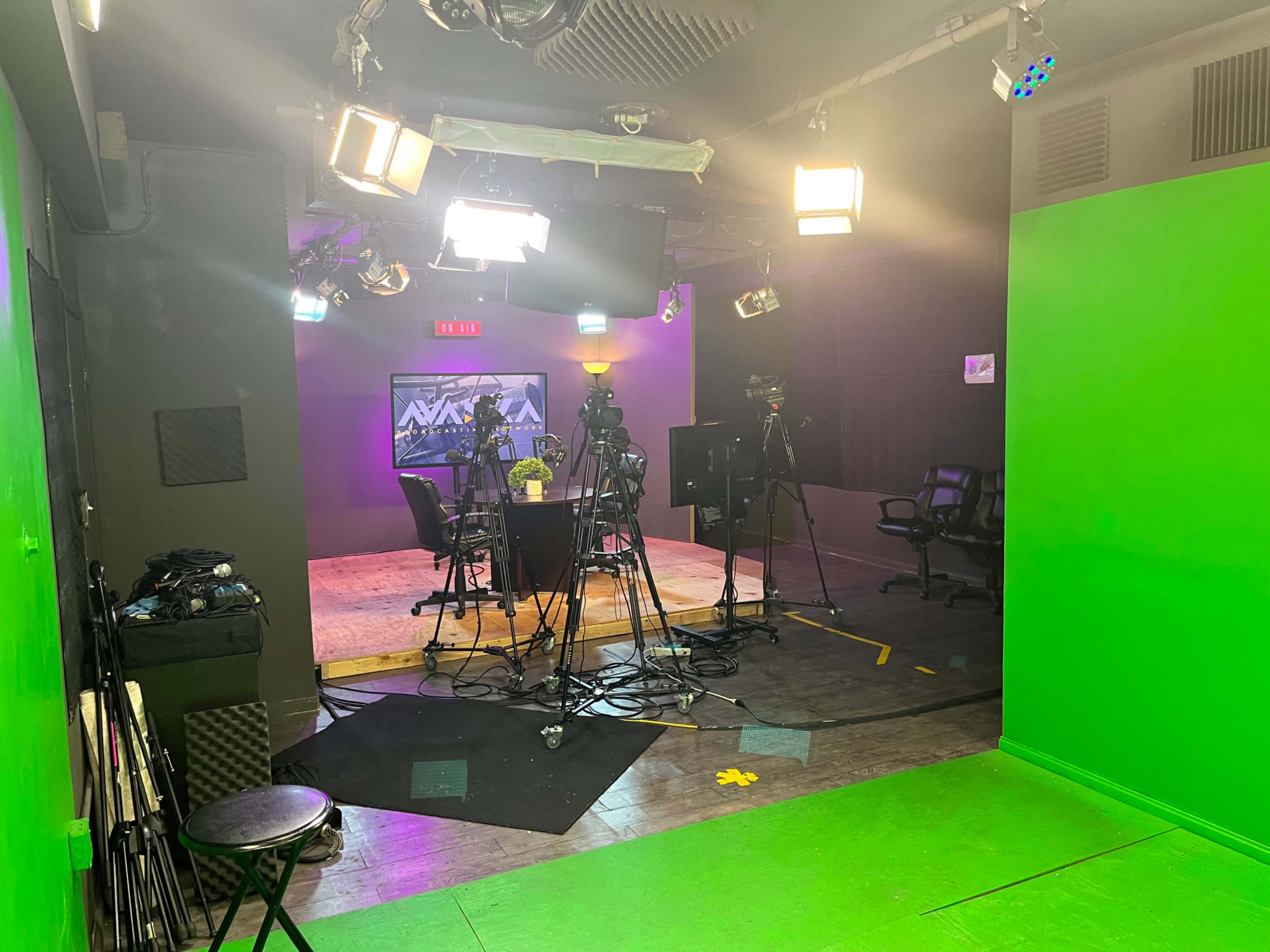 A television studio setup with multiple cameras, bright lights, and green walls, indicating a space prepared for video production.