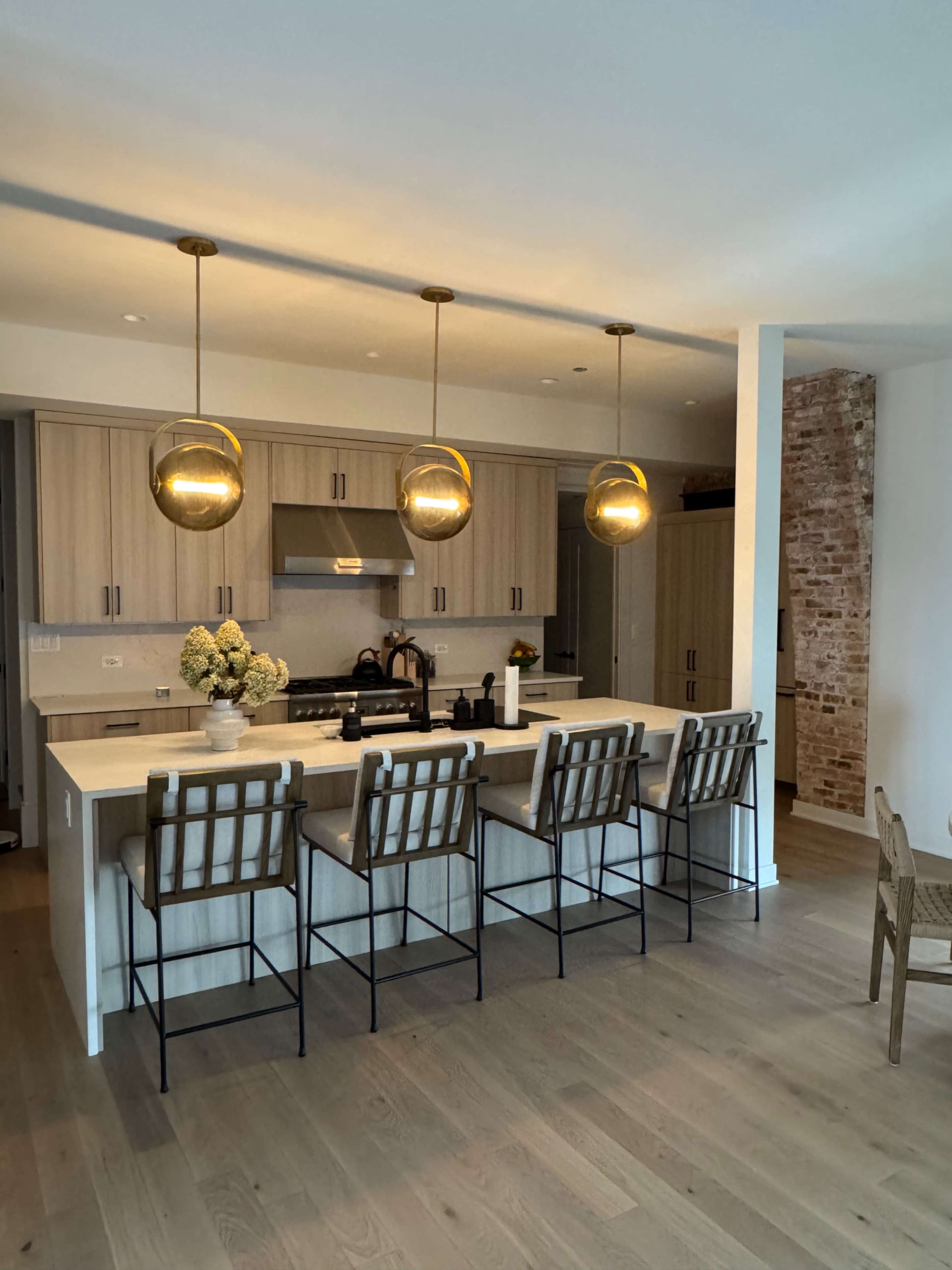 A modern kitchen features light wood cabinetry, a large island with seating for six, and three pendant lights hanging above.