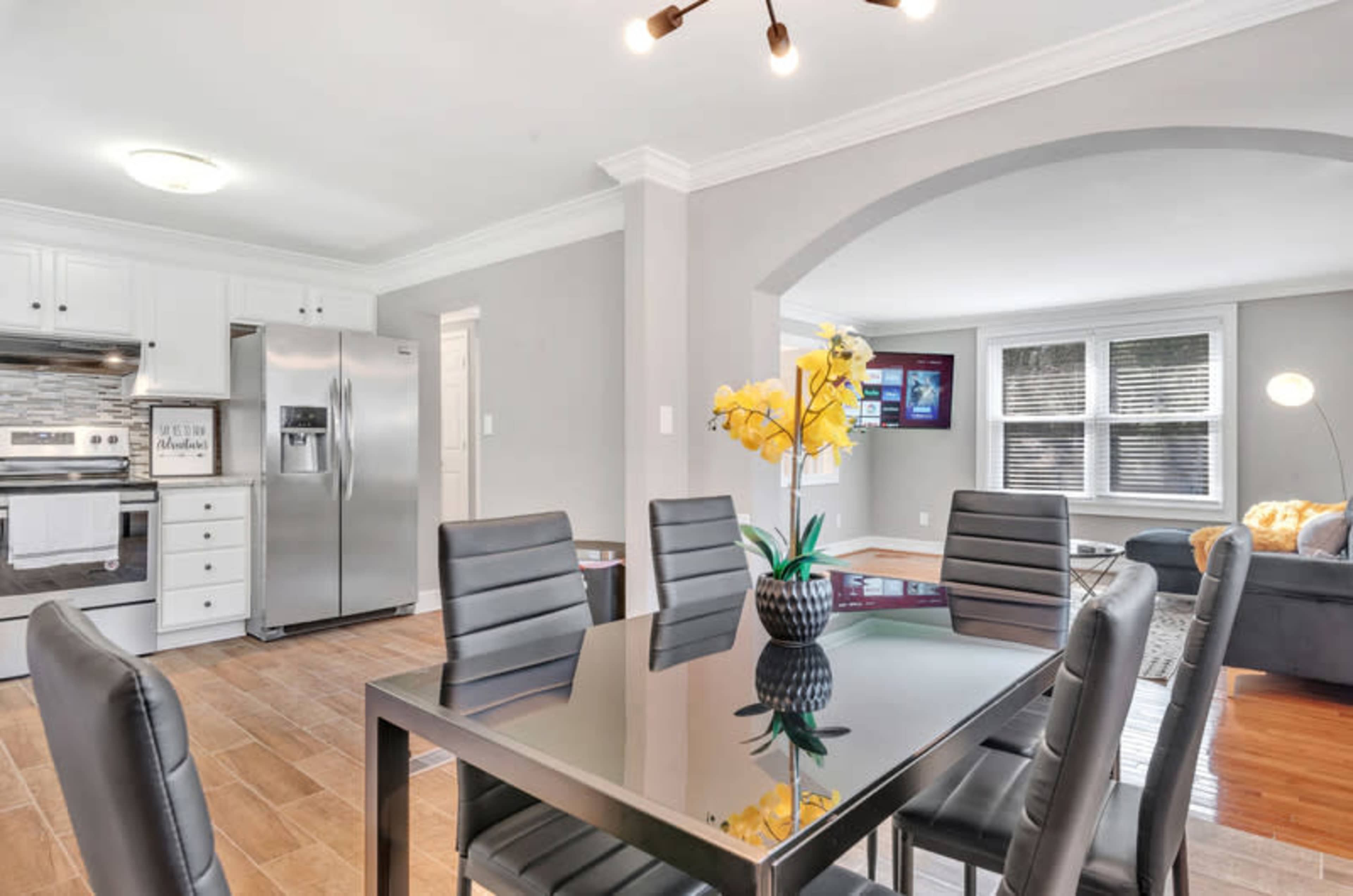 A modern dining area with a glass table and black chairs adjacent to a kitchen featuring stainless steel appliances.