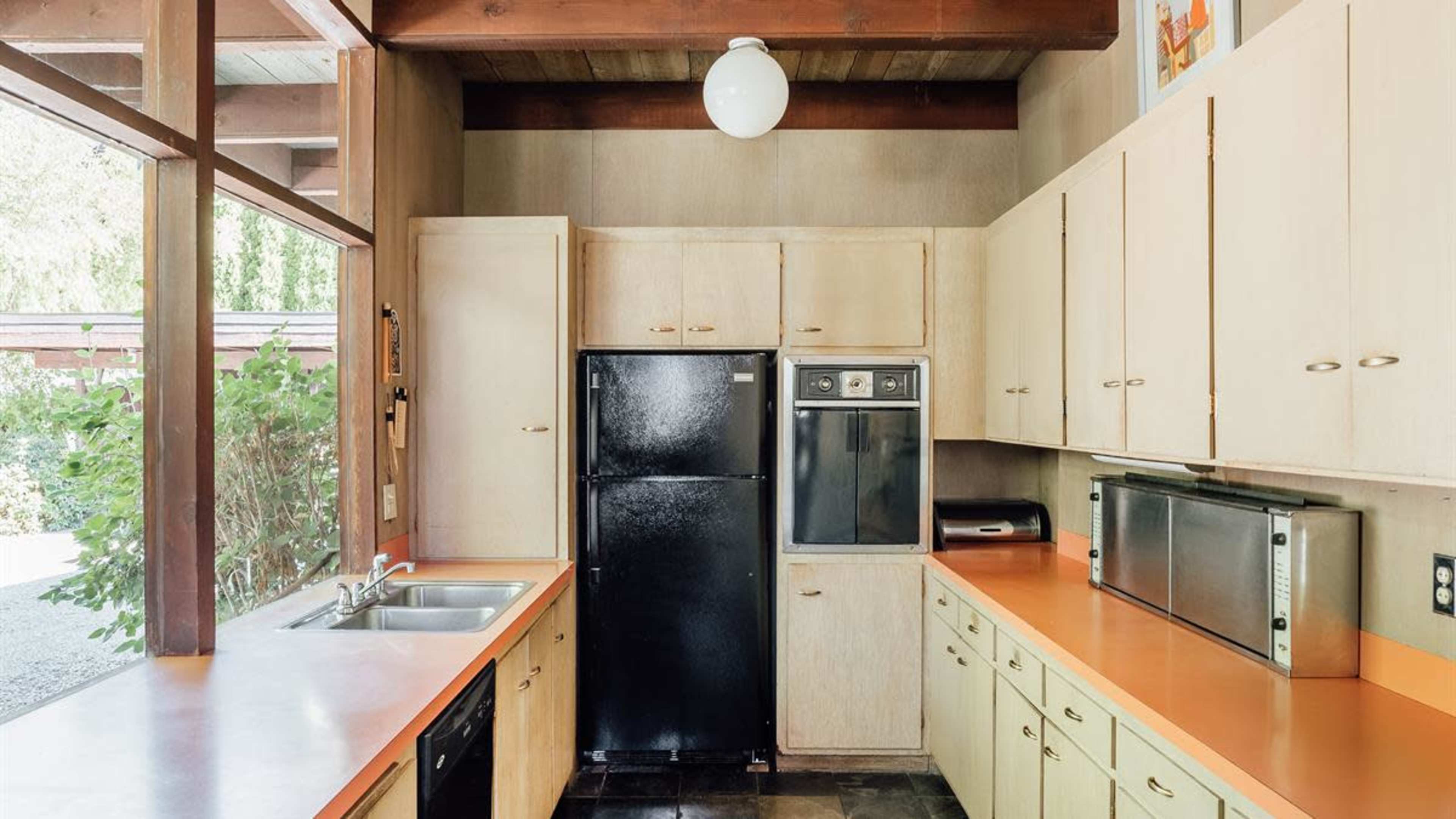 A modern kitchen with wooden beams, light-colored cabinetry, and appliances, including a black refrigerator and a stainless steel microwave.